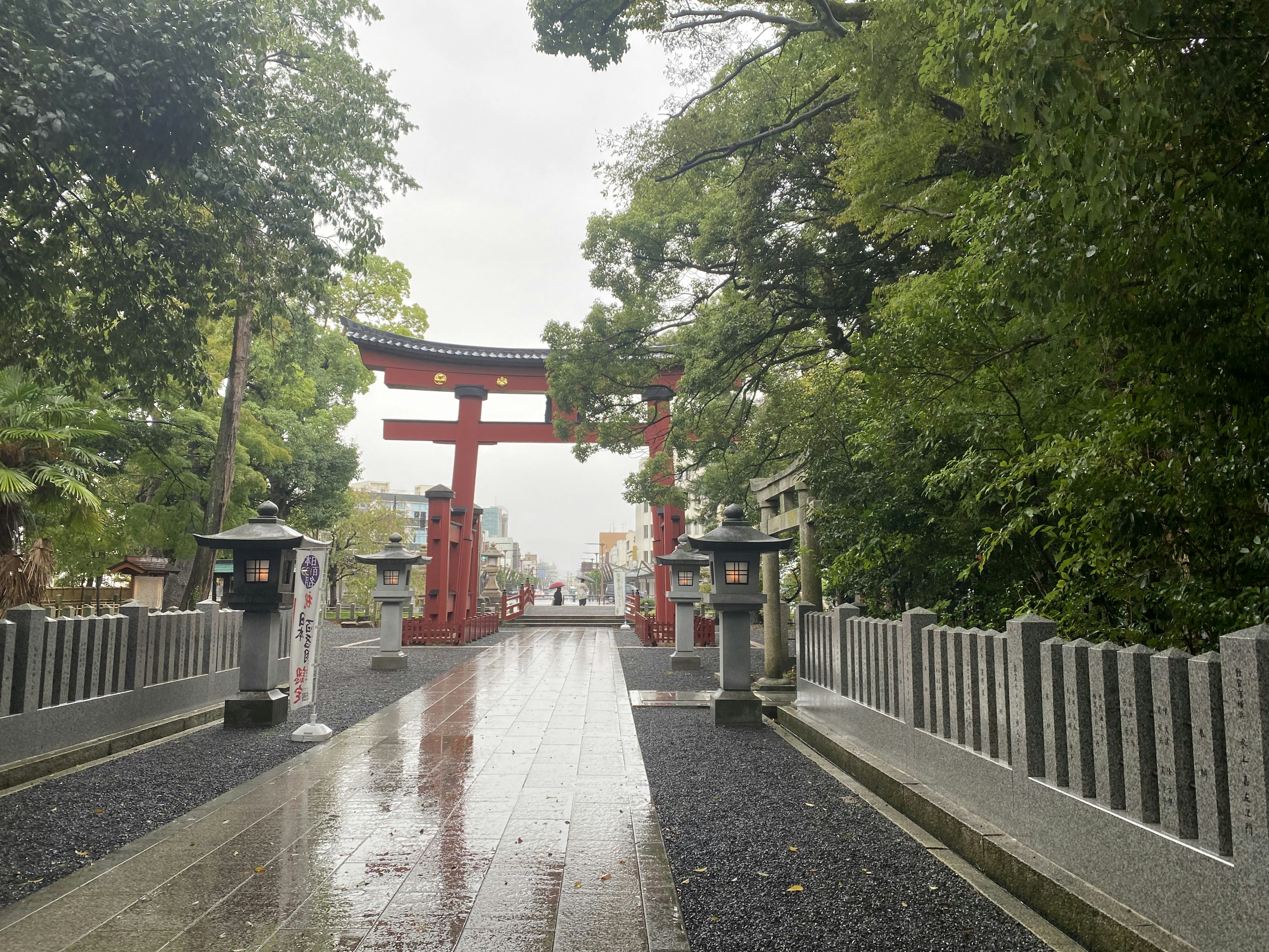 Con đường dẫn đến đền thờ với cổng torii đỏ và đèn đá mặt đường ướt và cây cối xanh tươi