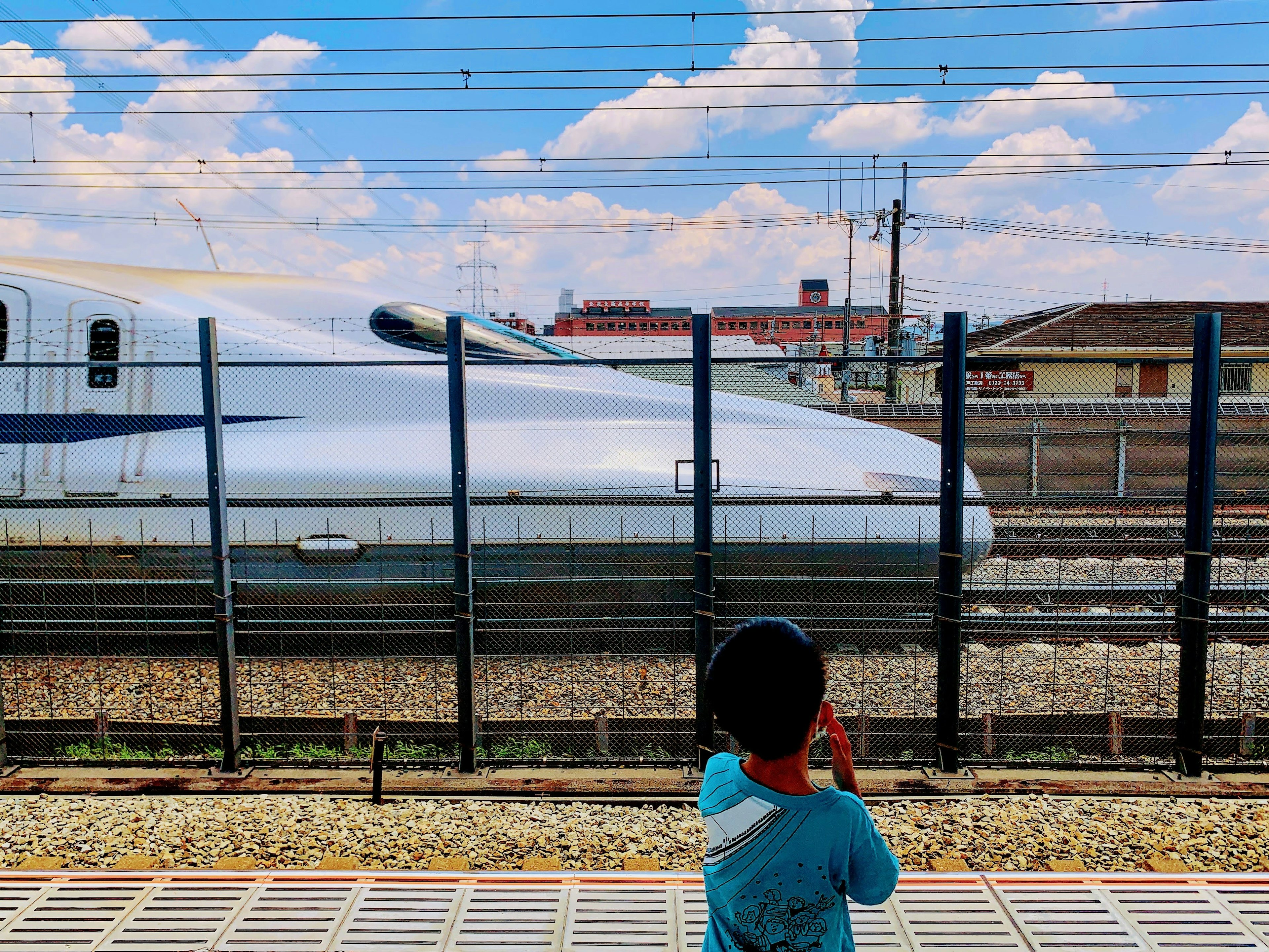 Kind beobachtet einen Shinkansen-Zug mit blauem Himmel und Wolken im Hintergrund