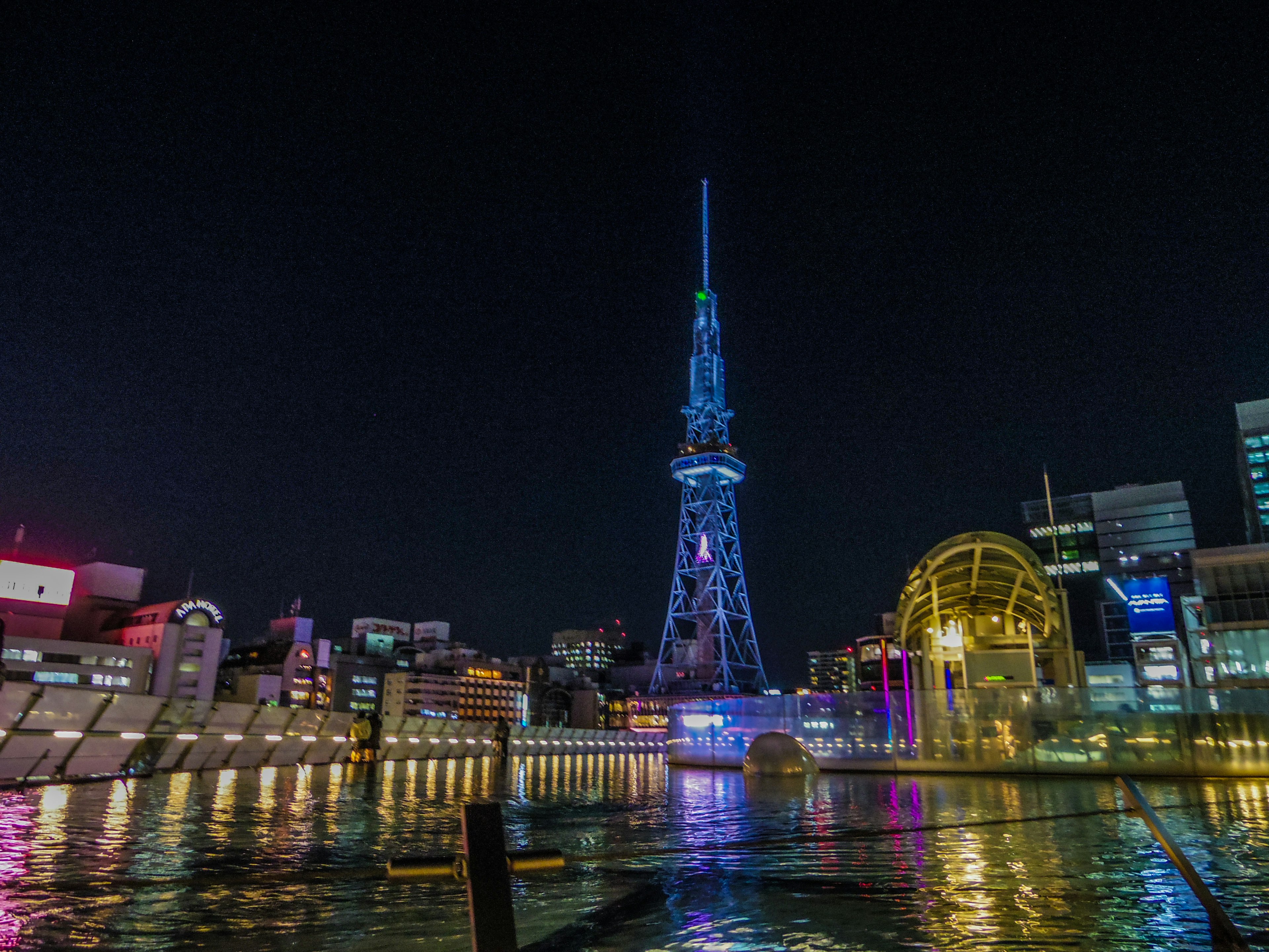 Torre della televisione di Nagoya illuminata di notte con riflessi colorati sull'acqua