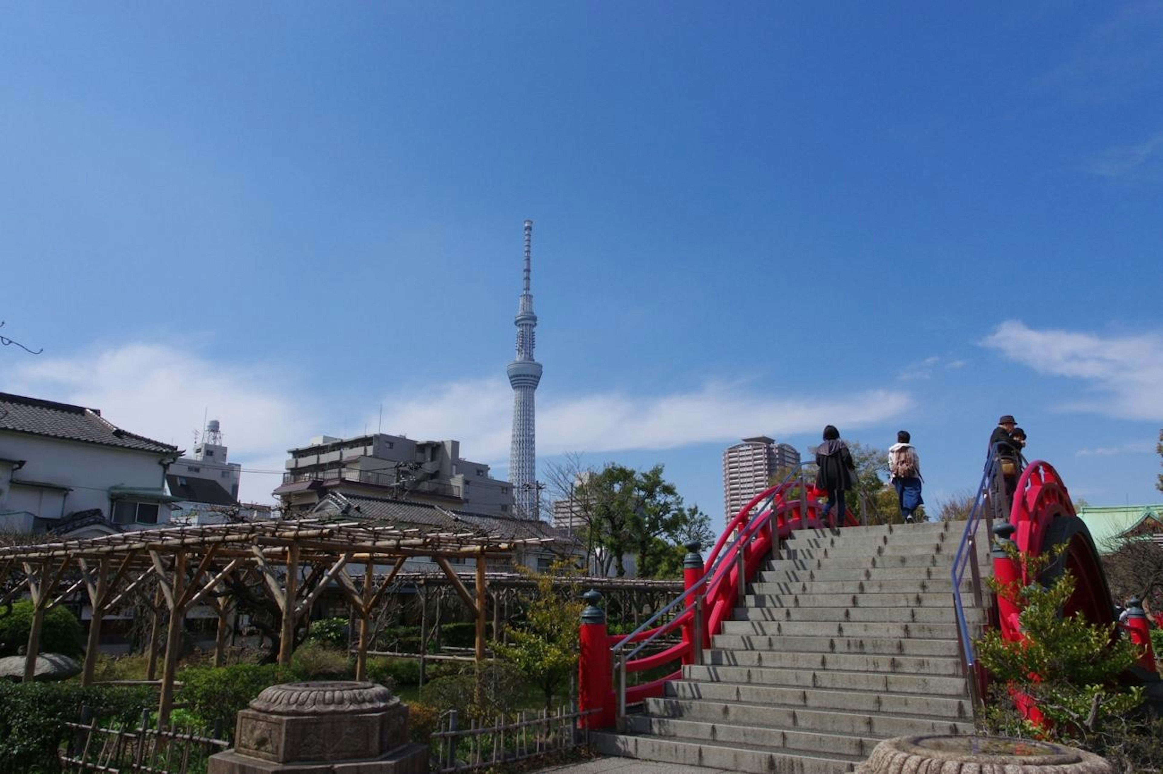 Pemandangan taman dengan jembatan merah dan Tokyo Skytree di latar belakang