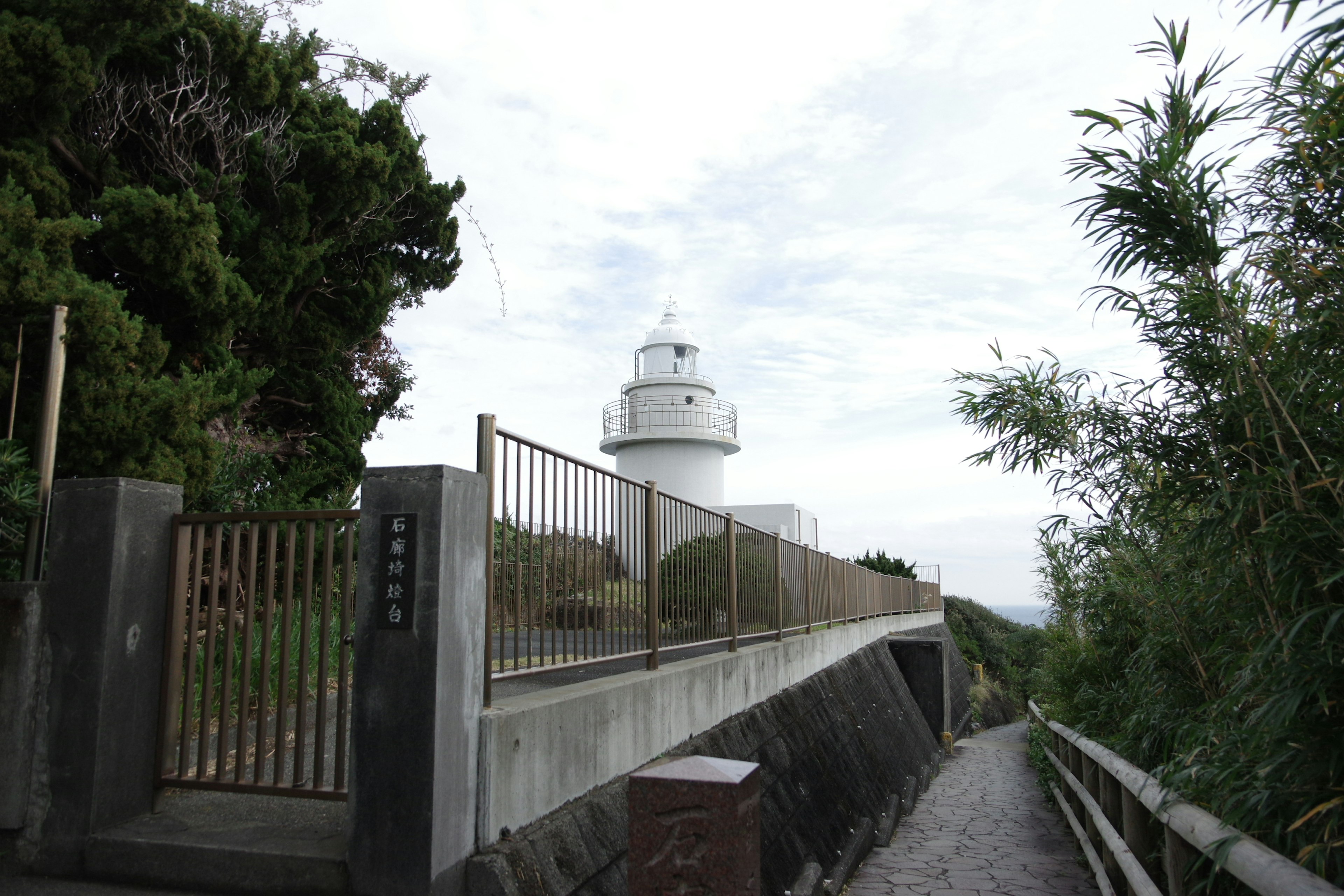 Weißer Leuchtturm umgeben von Grün und bewölktem Himmel