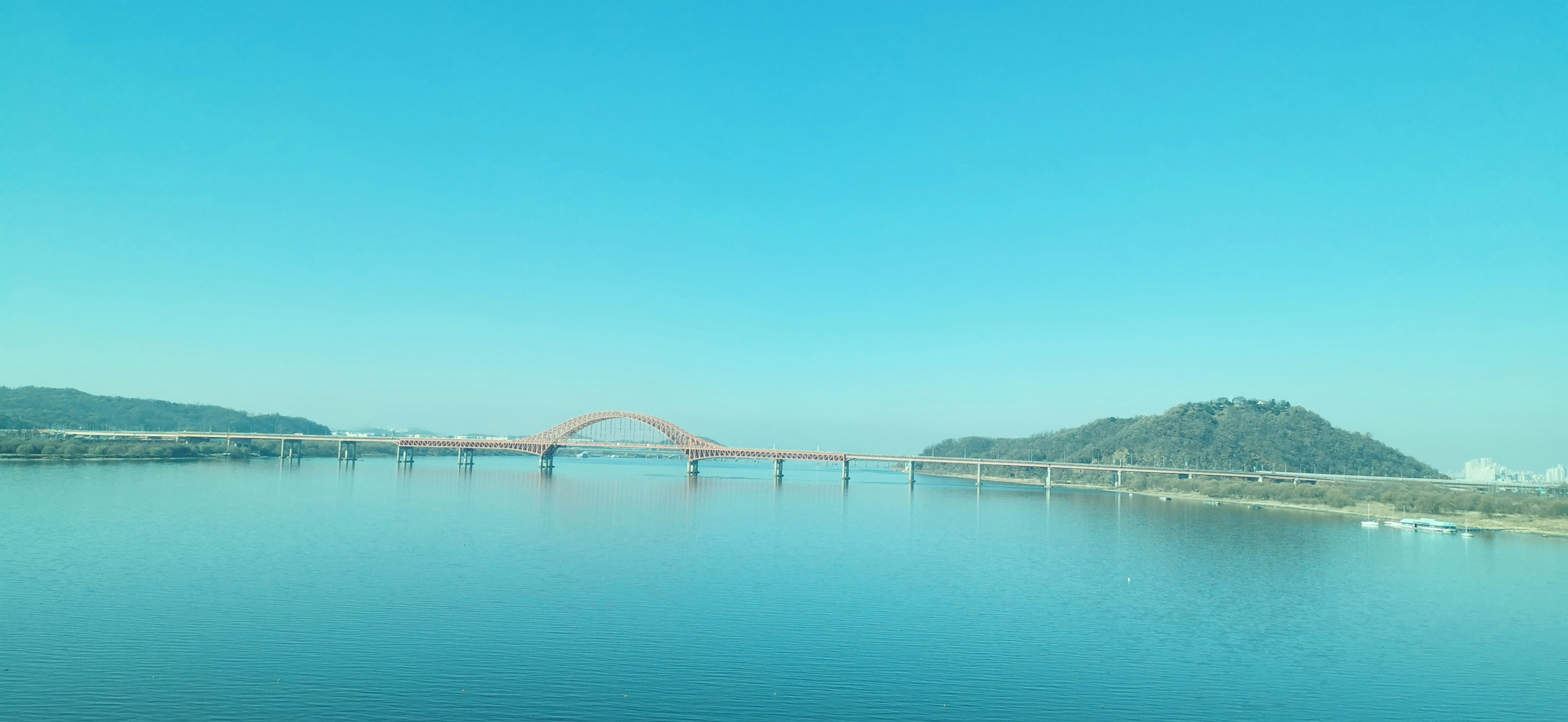 Pemandangan jembatan merah di atas air tenang dengan langit biru