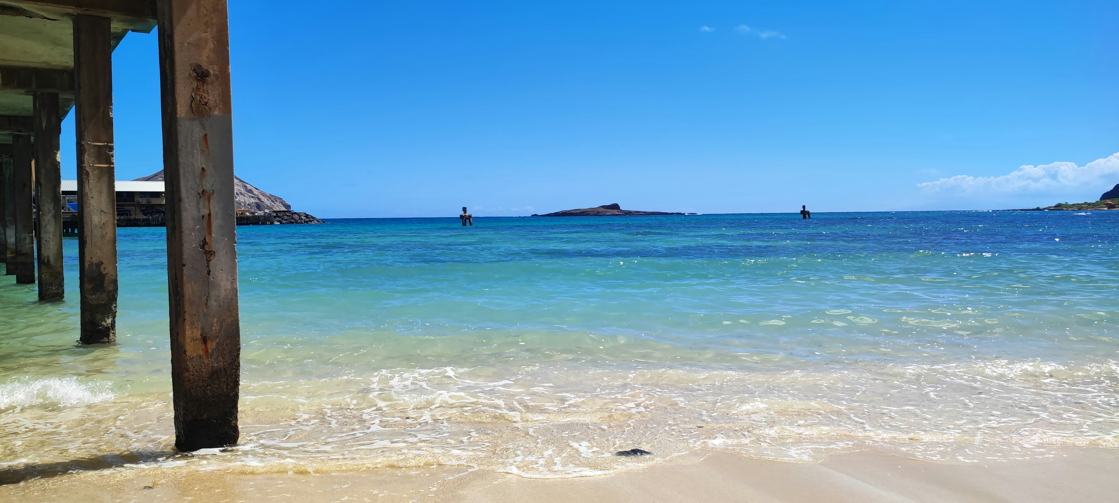 Vista panoramica dell'oceano blu chiaro e della spiaggia di sabbia con colonne di legno di un molo