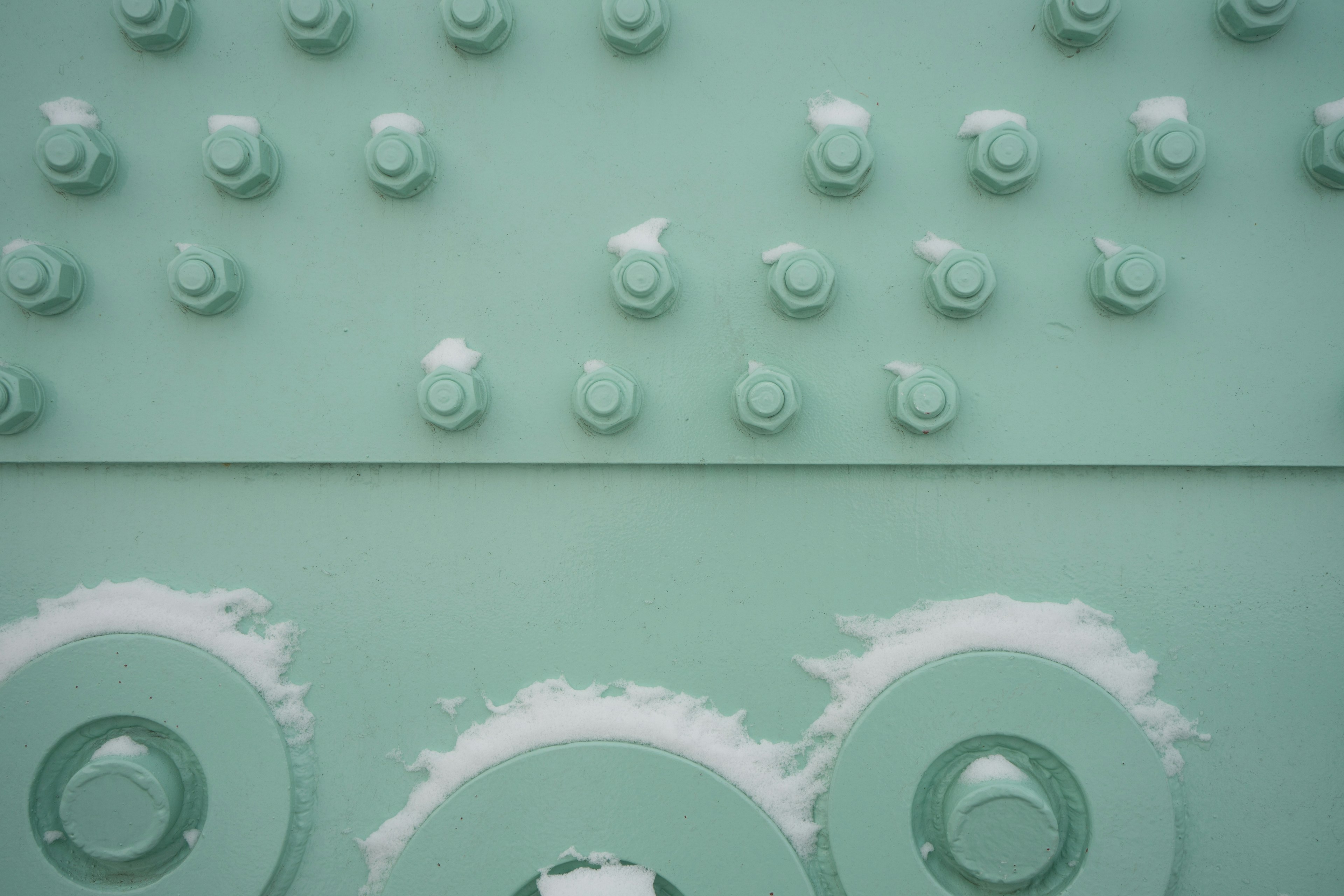 Light green metal surface with rows of bolts and circular patterns