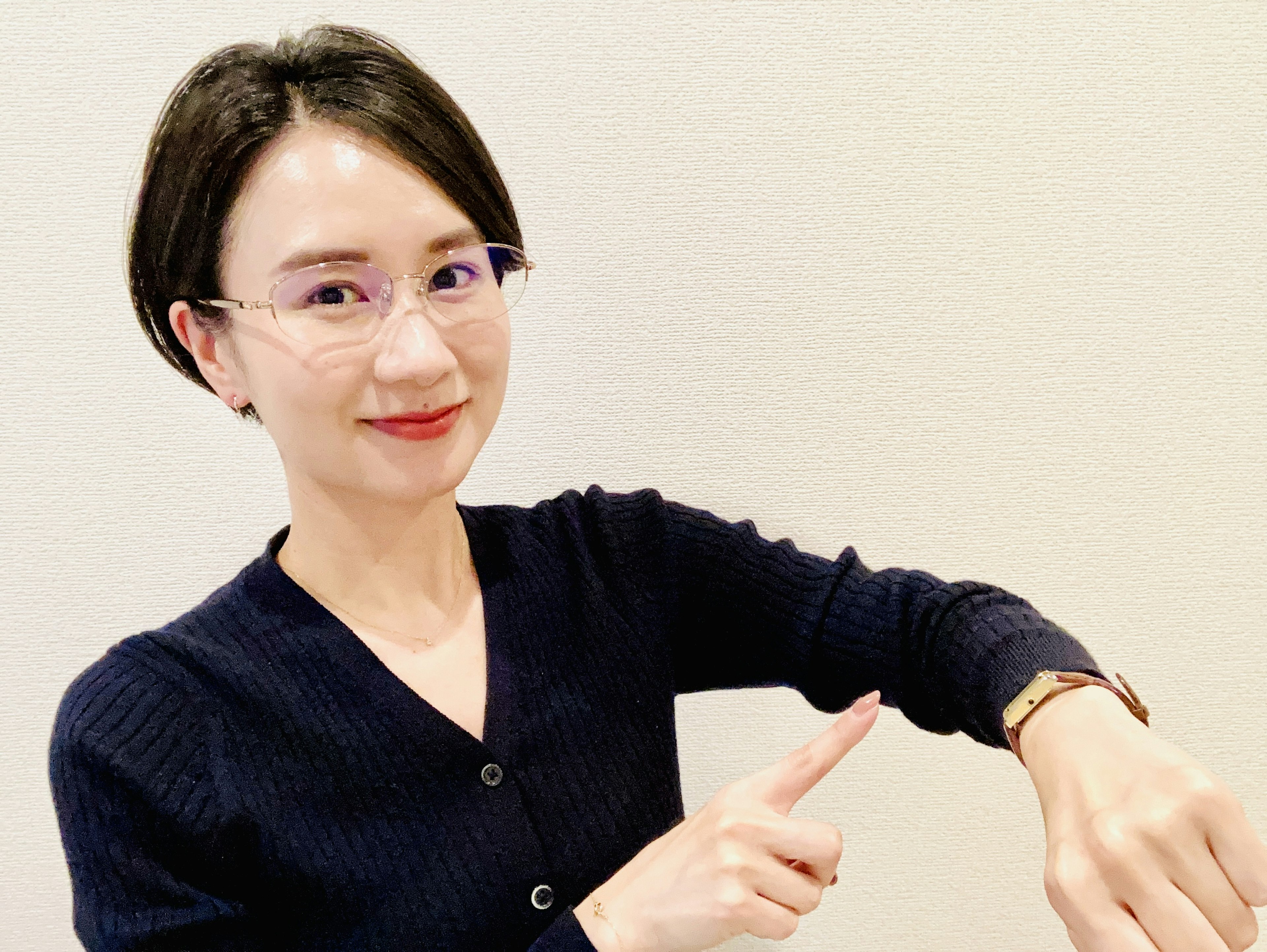 A woman in a black sweater pointing at a wristwatch