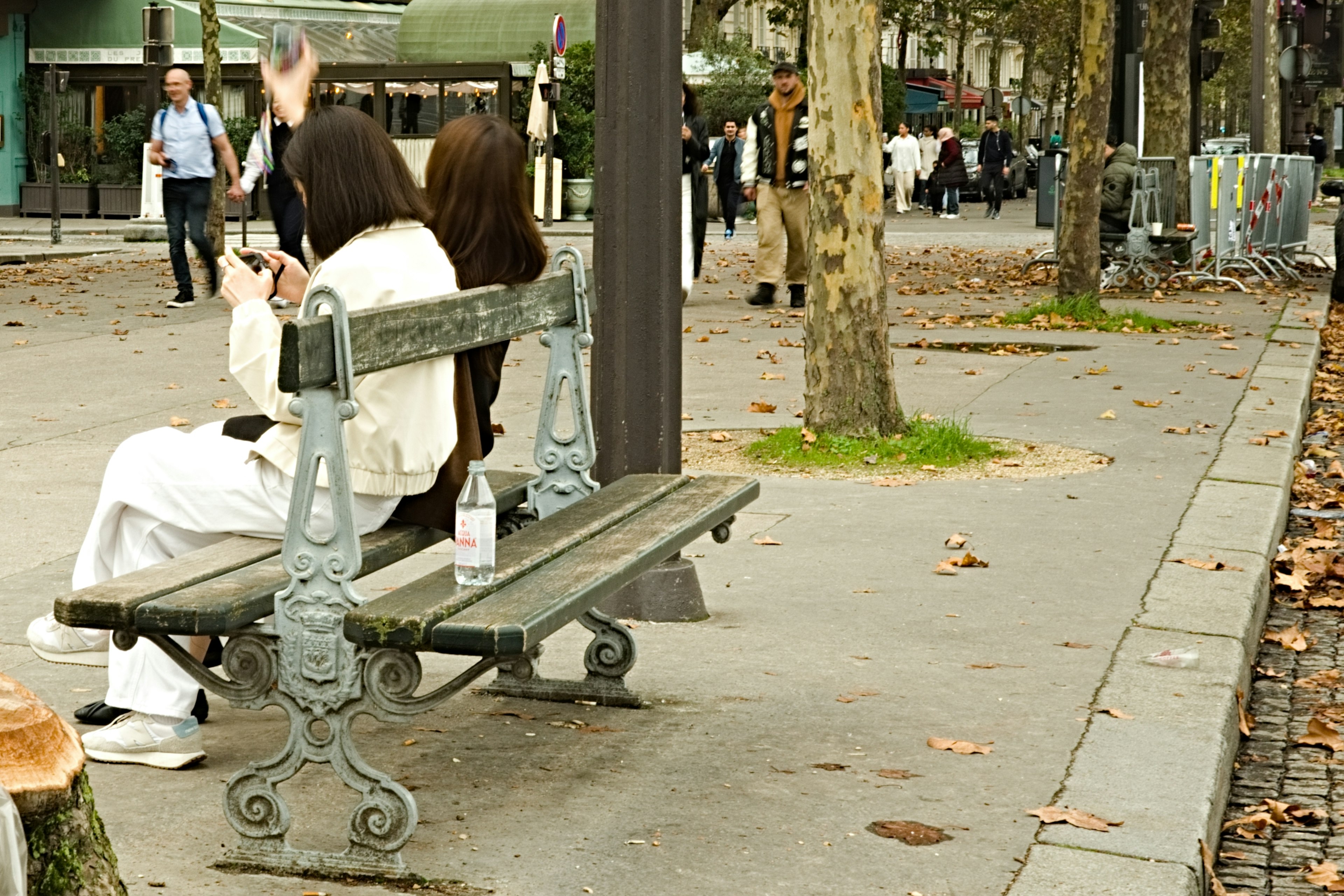 Zwei Frauen sitzen auf einer Parkbank mit Passanten im Hintergrund