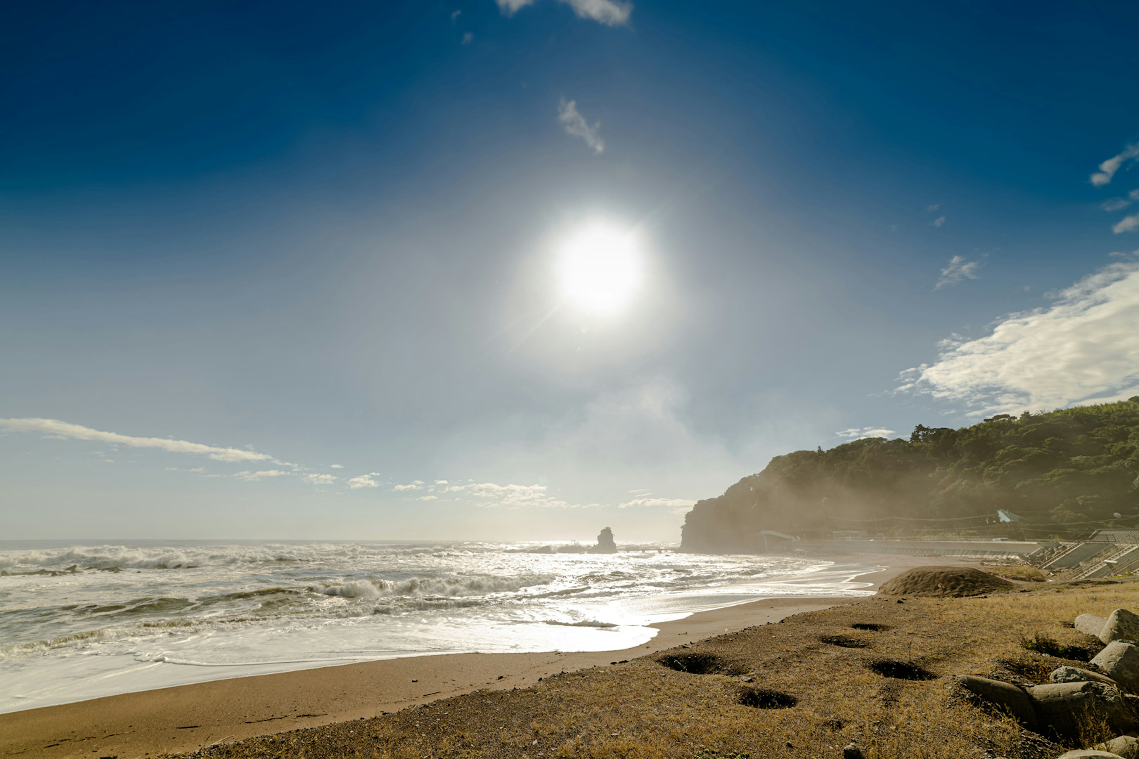 Paesaggio costiero con cielo blu e sole splendente onde che si infrangono sulla spiaggia sabbiosa