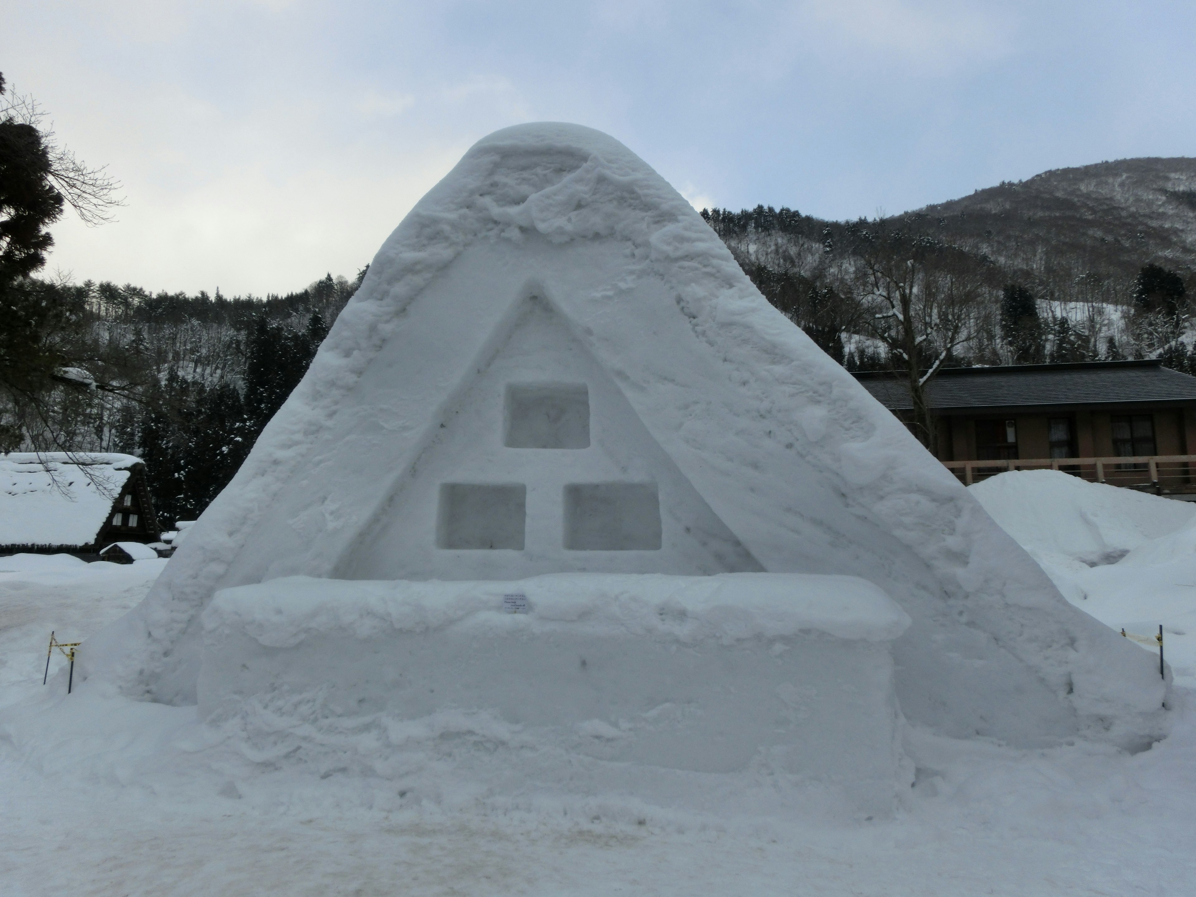 Escultura de nieve de una cabaña triangular rodeada de un paisaje nevado