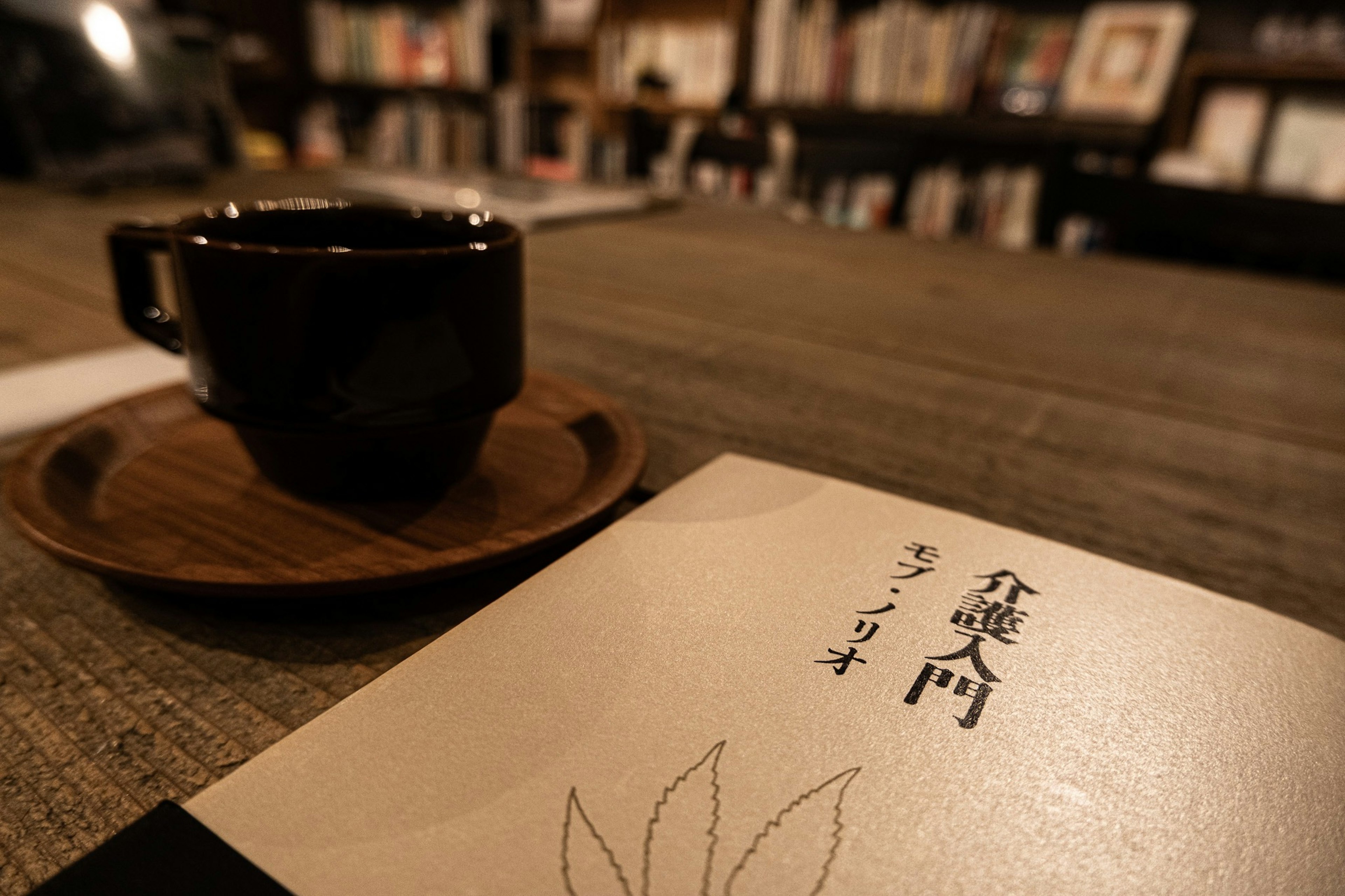 Une tasse noire sur une soucoupe en bois posée sur une table avec un livre