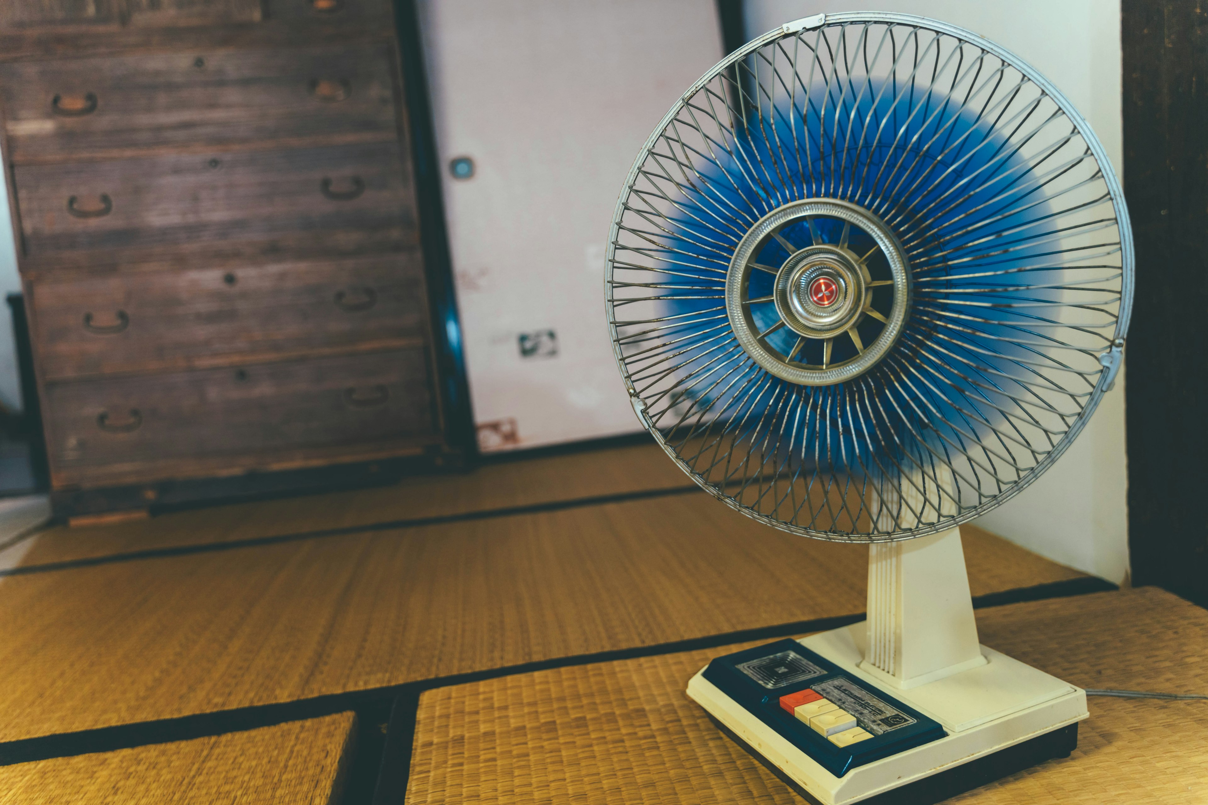 Un ventilatore retrò con pale blu posizionato su un pavimento in tatami