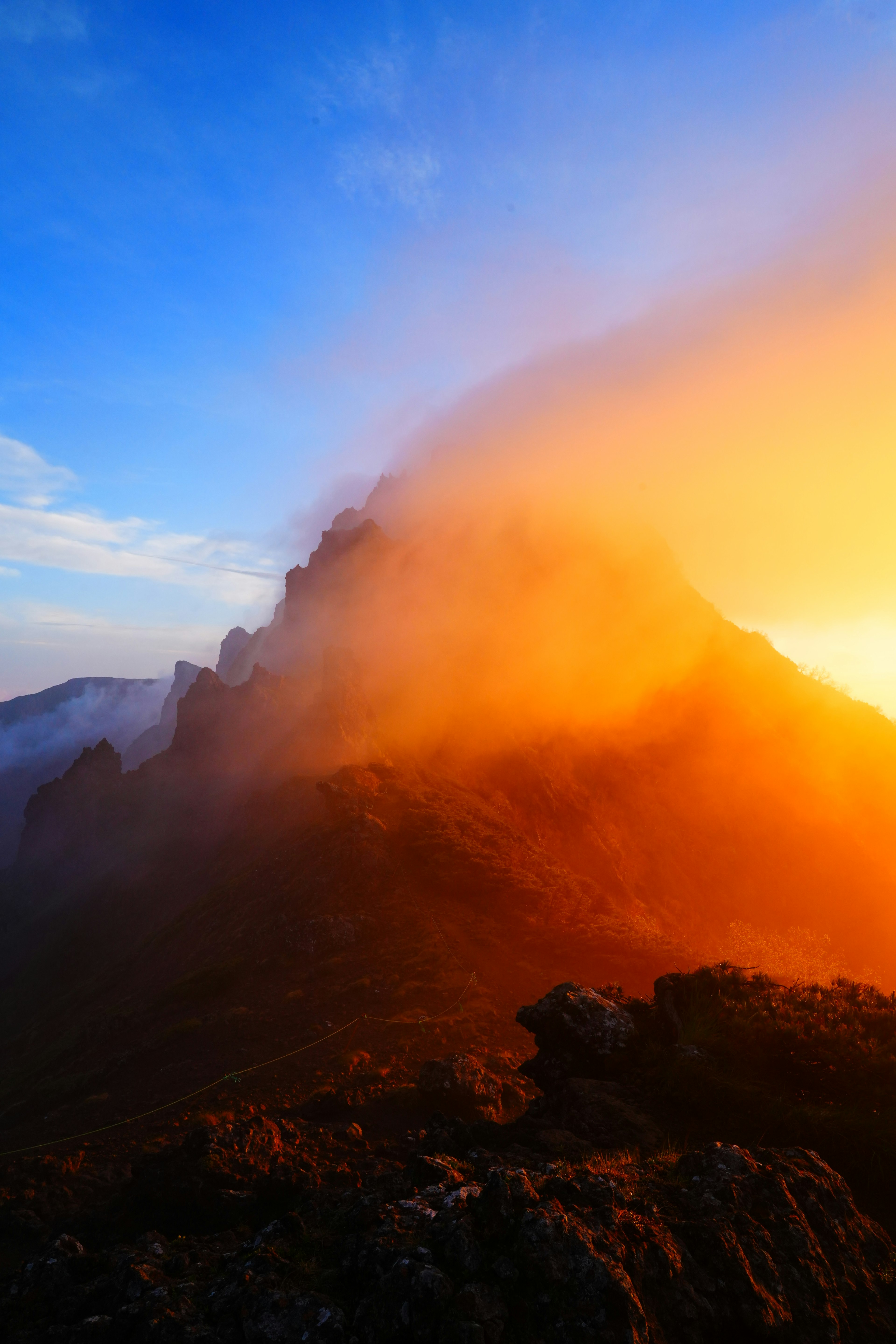 Puncak gunung yang diselimuti kabut disinari cahaya oranye saat matahari terbenam