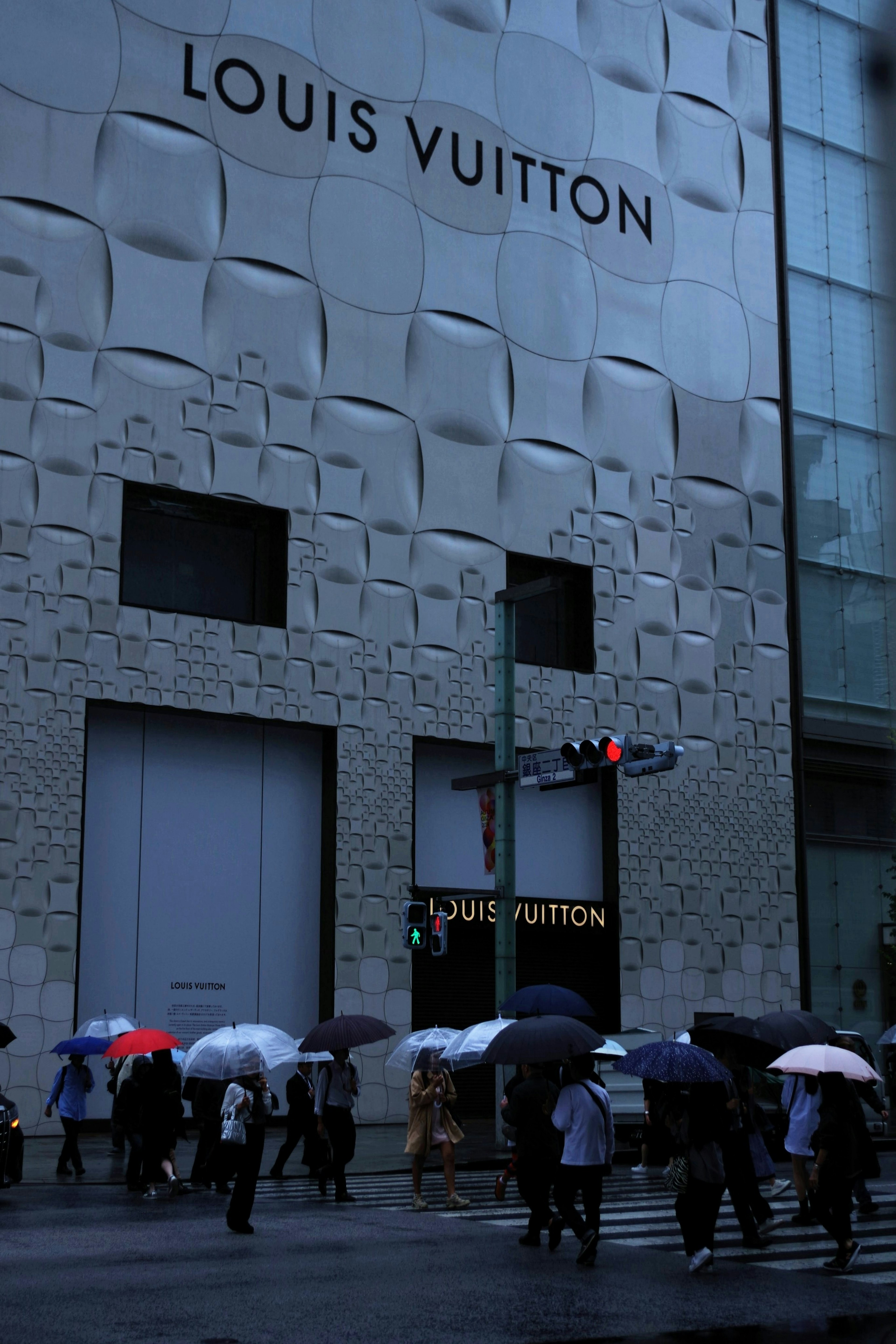 Menschen mit Regenschirmen, die vor einem Louis Vuitton Geschäft auf der Straße gehen