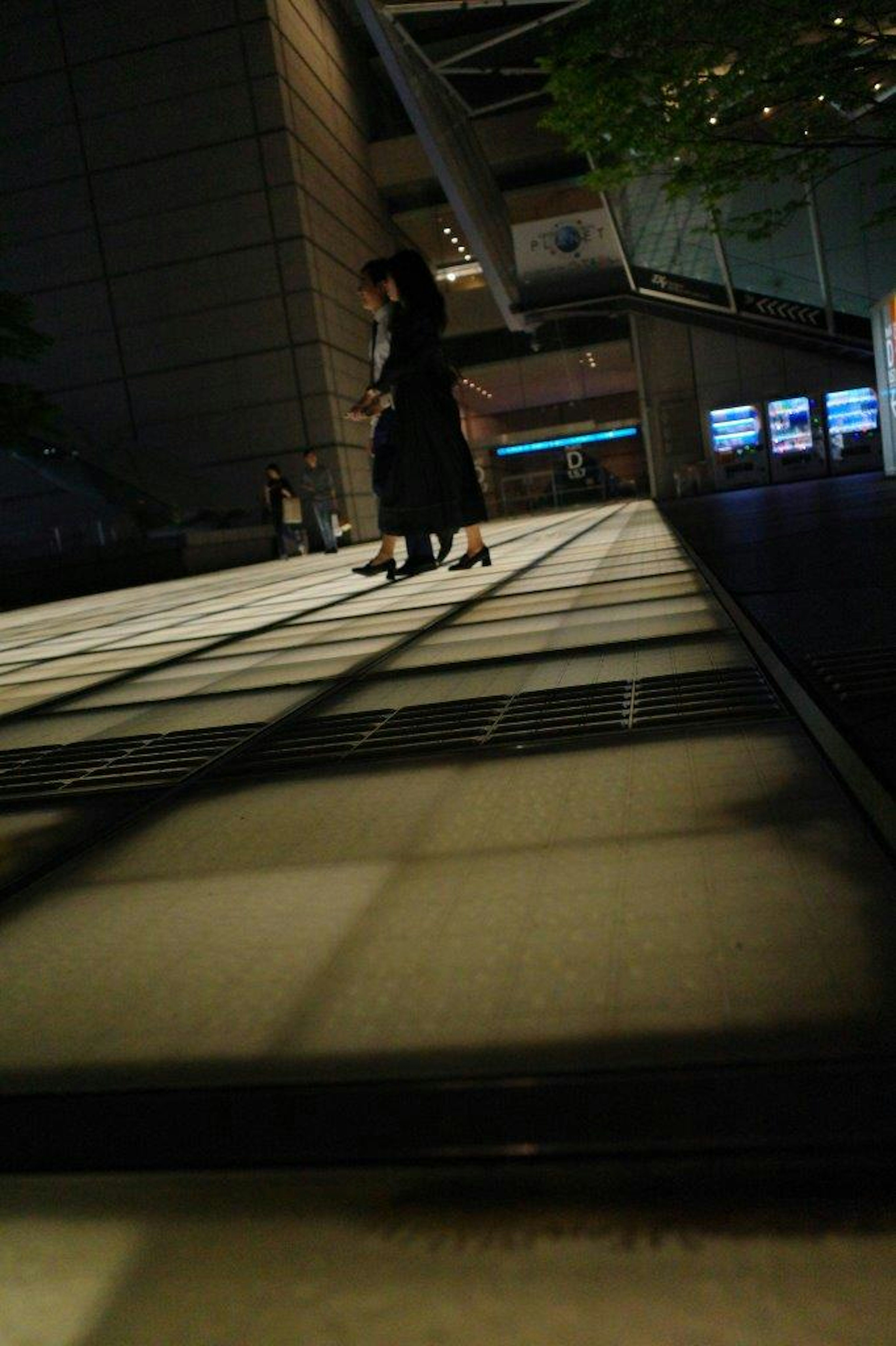 Silhouette einer Frau, die nachts auf einem Bürgersteig in der Stadt geht helle Fliesenreflexionen