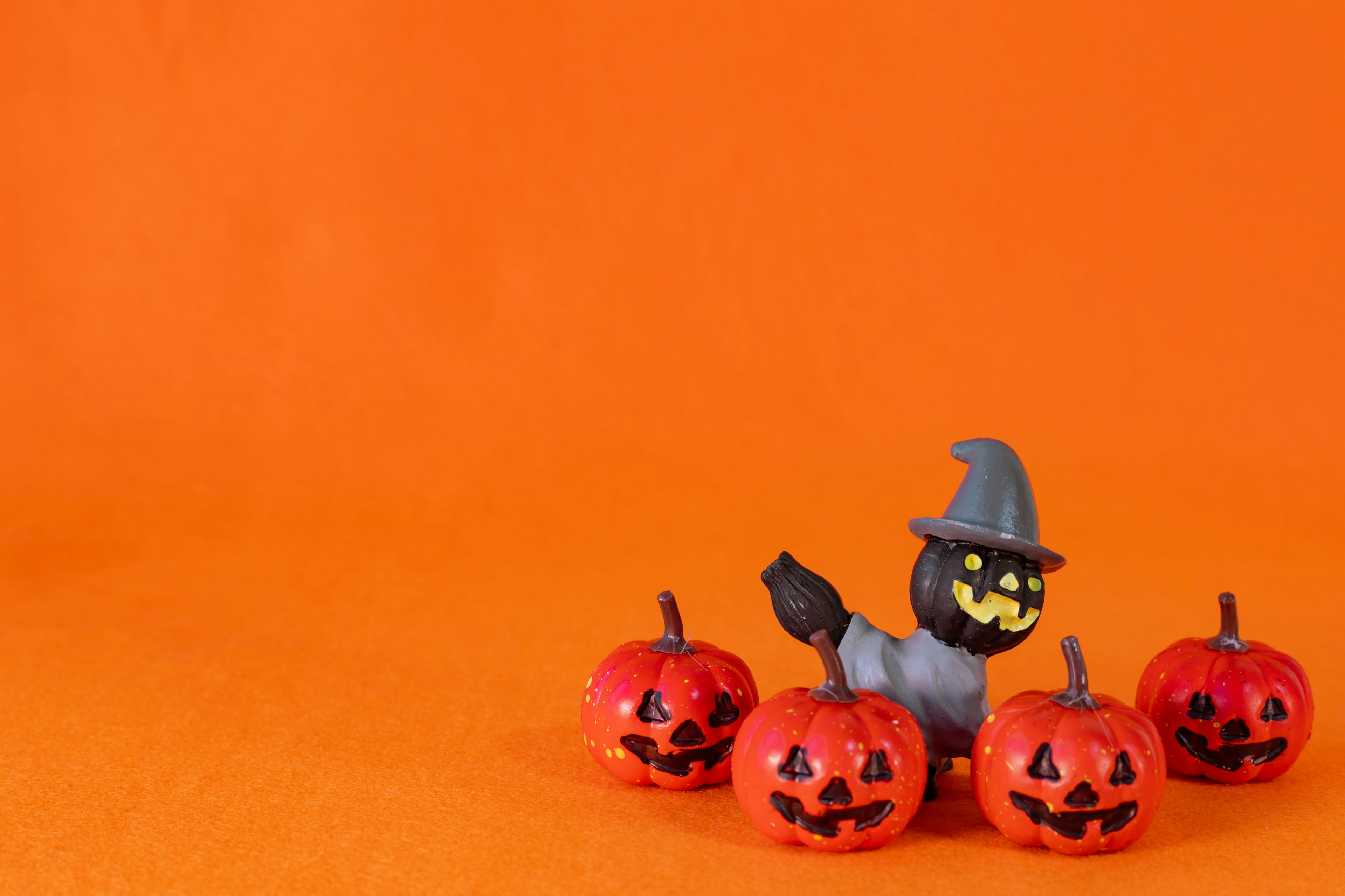 Red pumpkins with carved faces and a witch figurine on an orange background