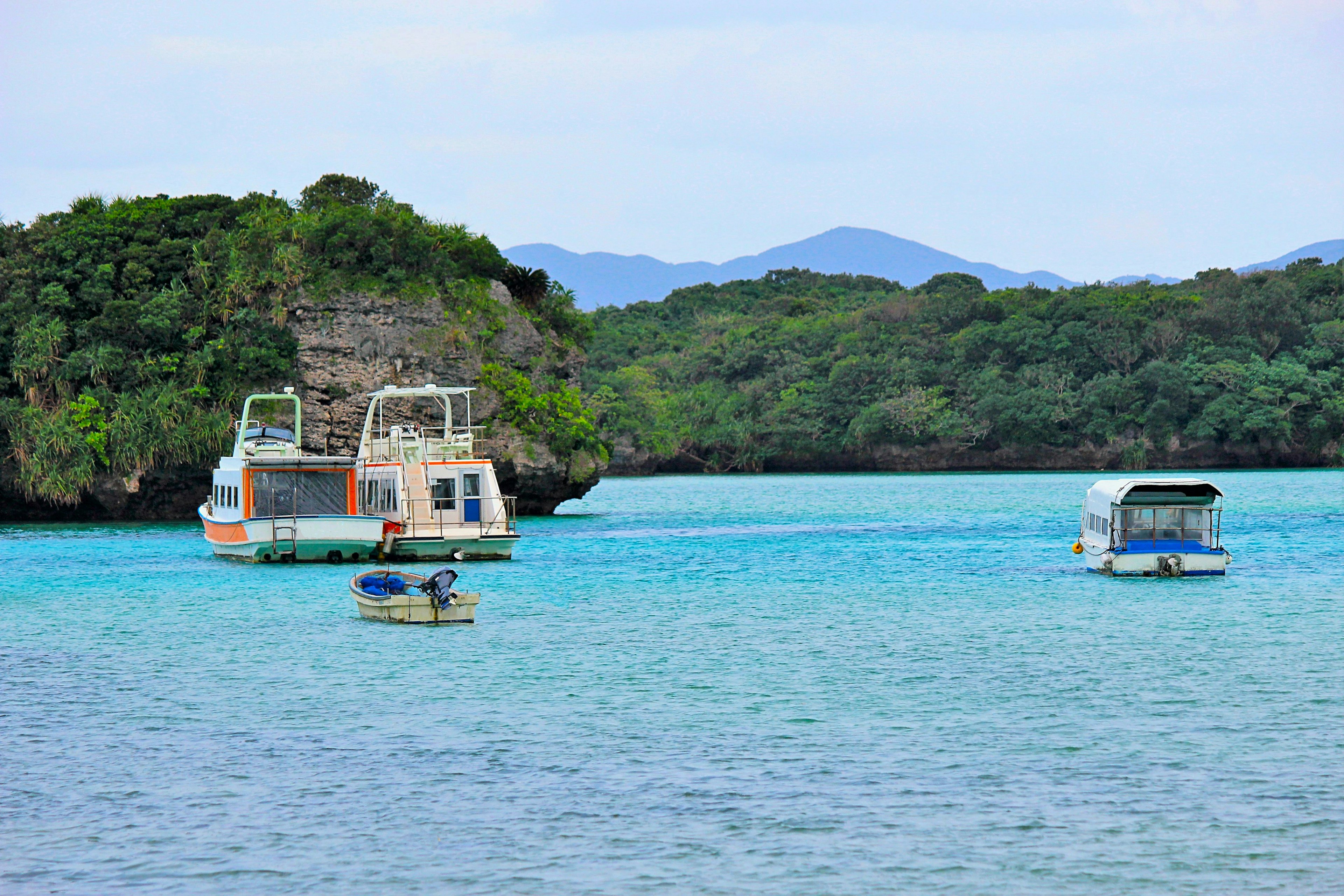 เรือหลายลำลอยอยู่บนผืนน้ำสีน้ำเงินสวยงามล้อมรอบด้วยความเขียวขจี