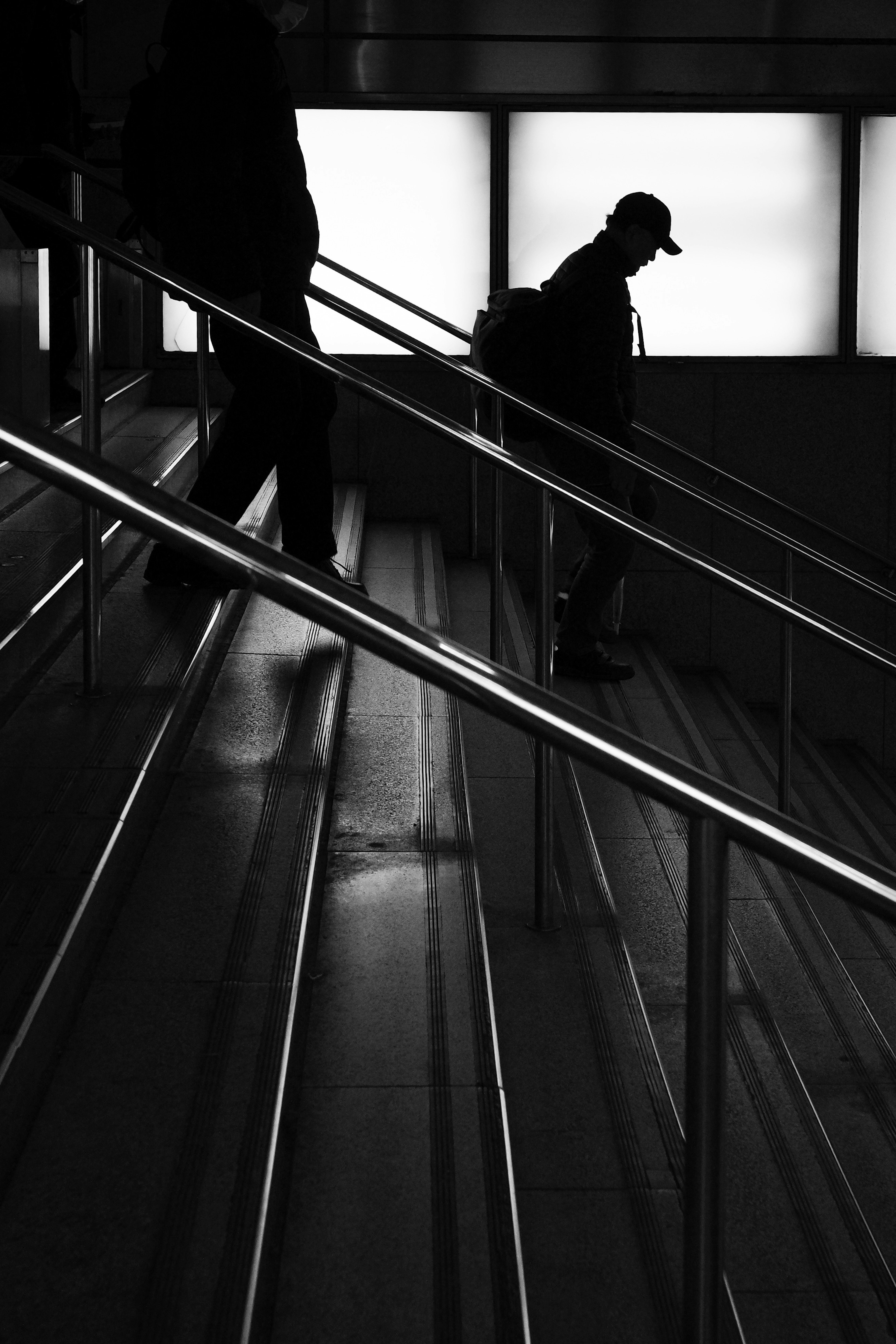 Silhouette of a person descending stairs with reflections on the railing in a monochrome image