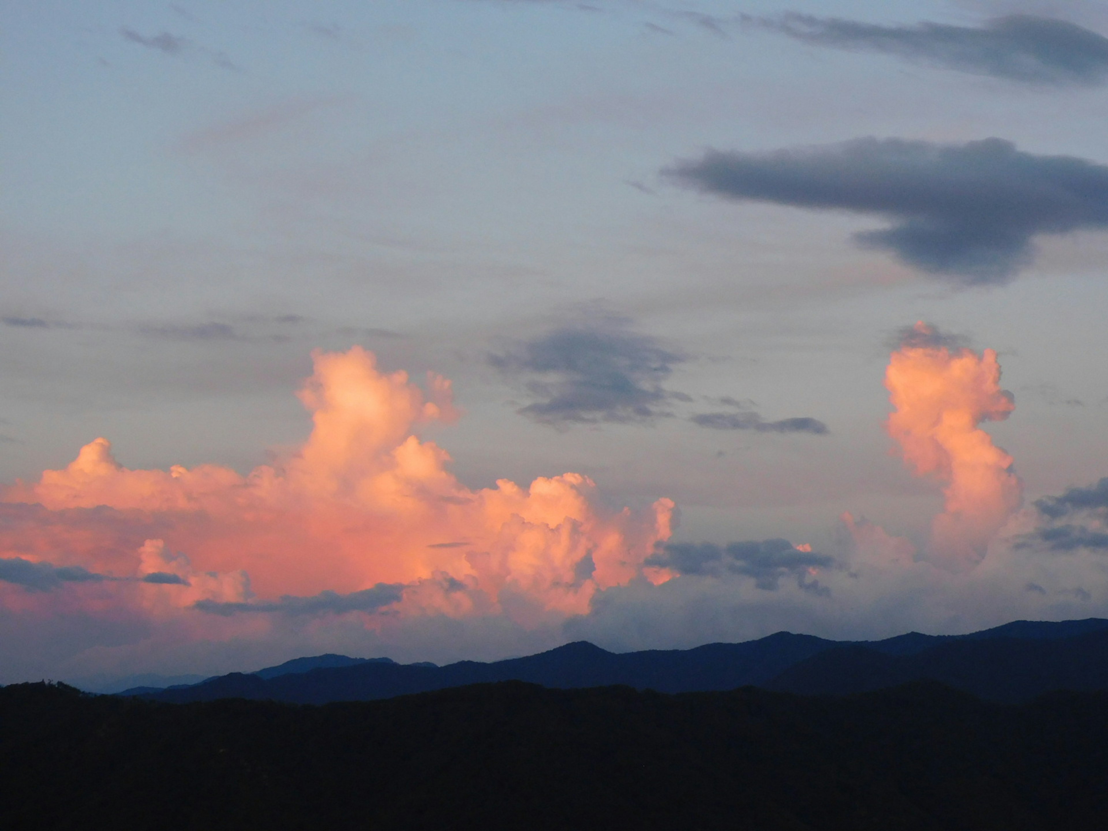 Sunset clouds illuminated with shades of pink over mountains