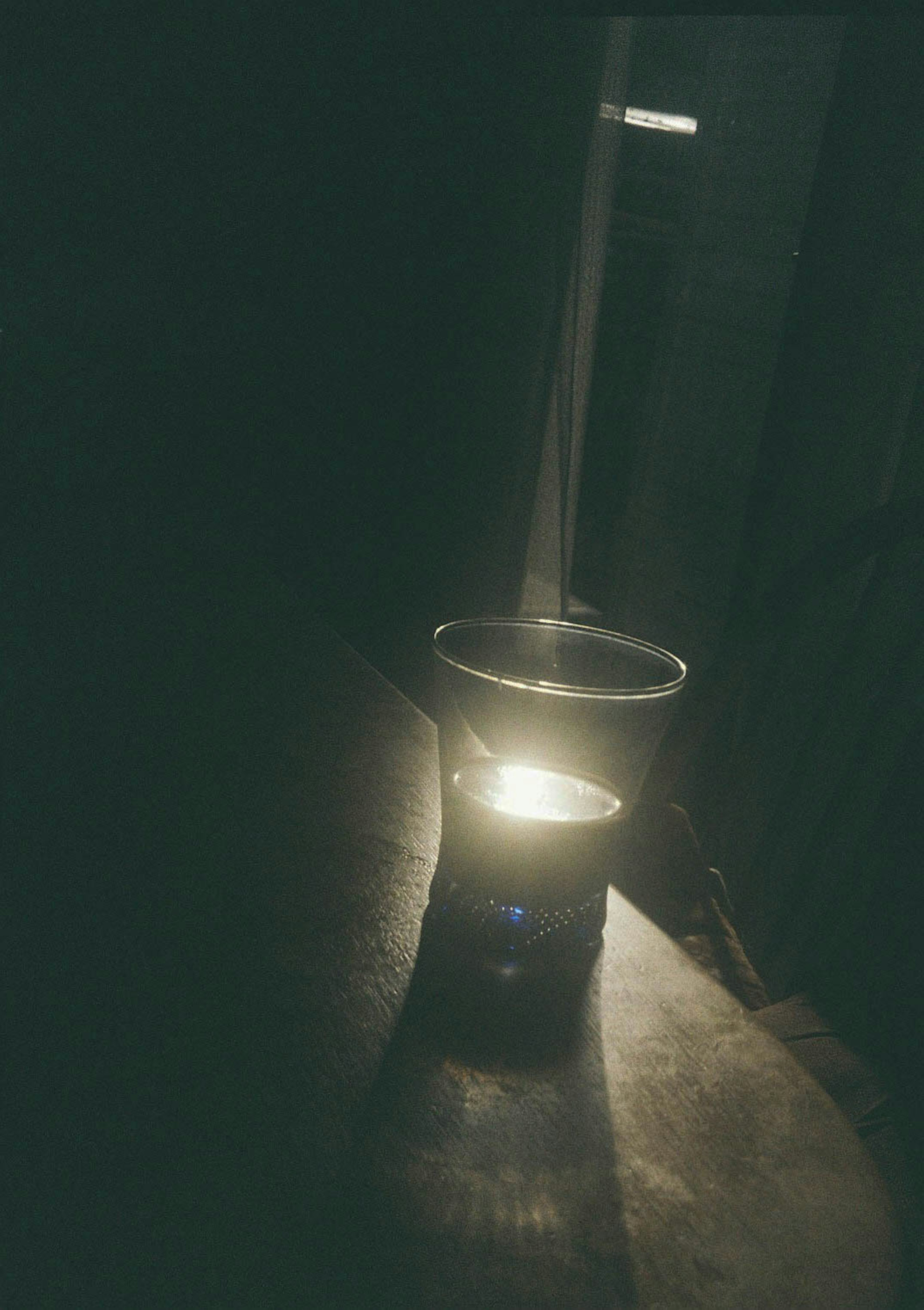 Vela en un vaso brillando suavemente contra un fondo oscuro