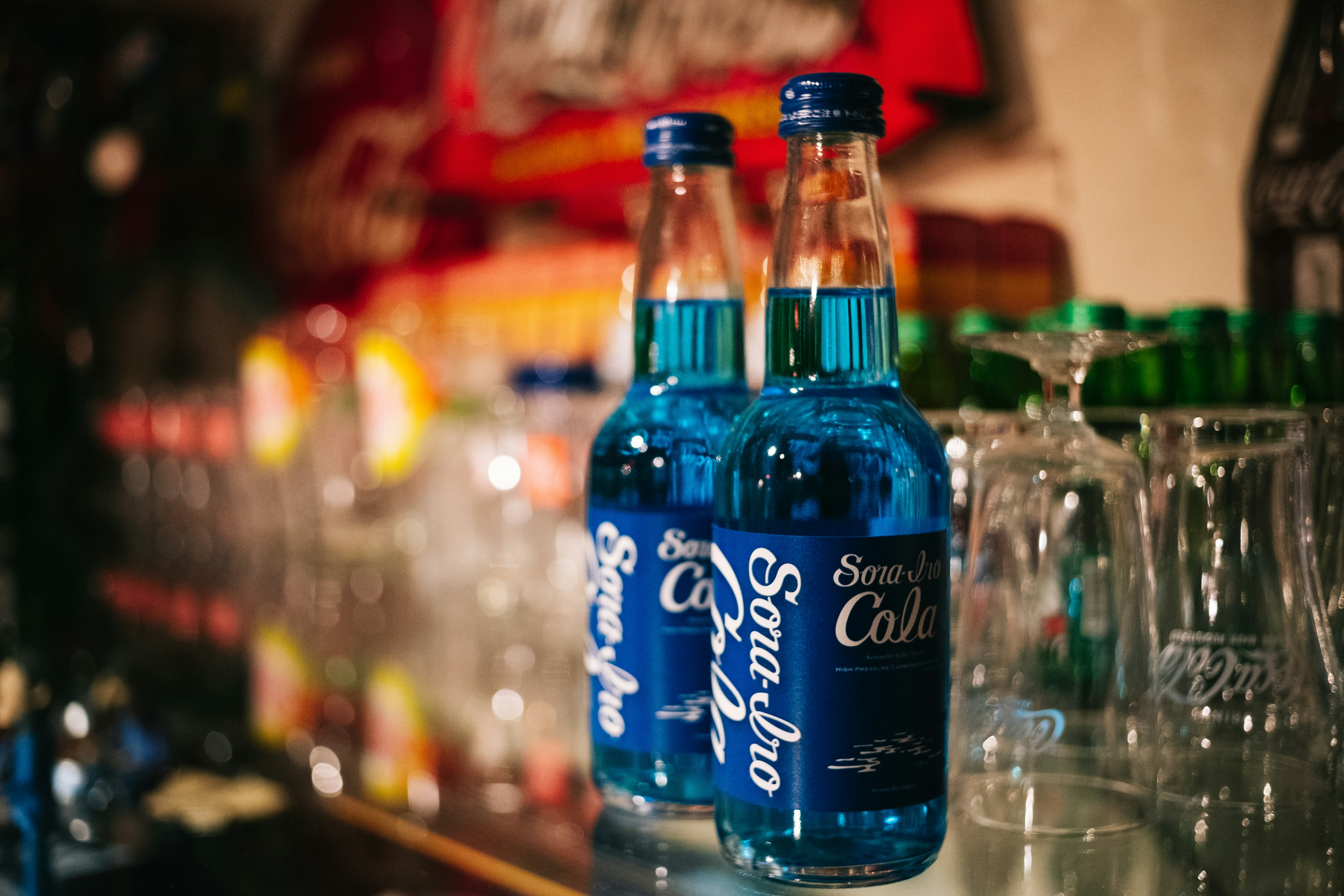 Two blue soda bottles on a bar counter with glassware in the background