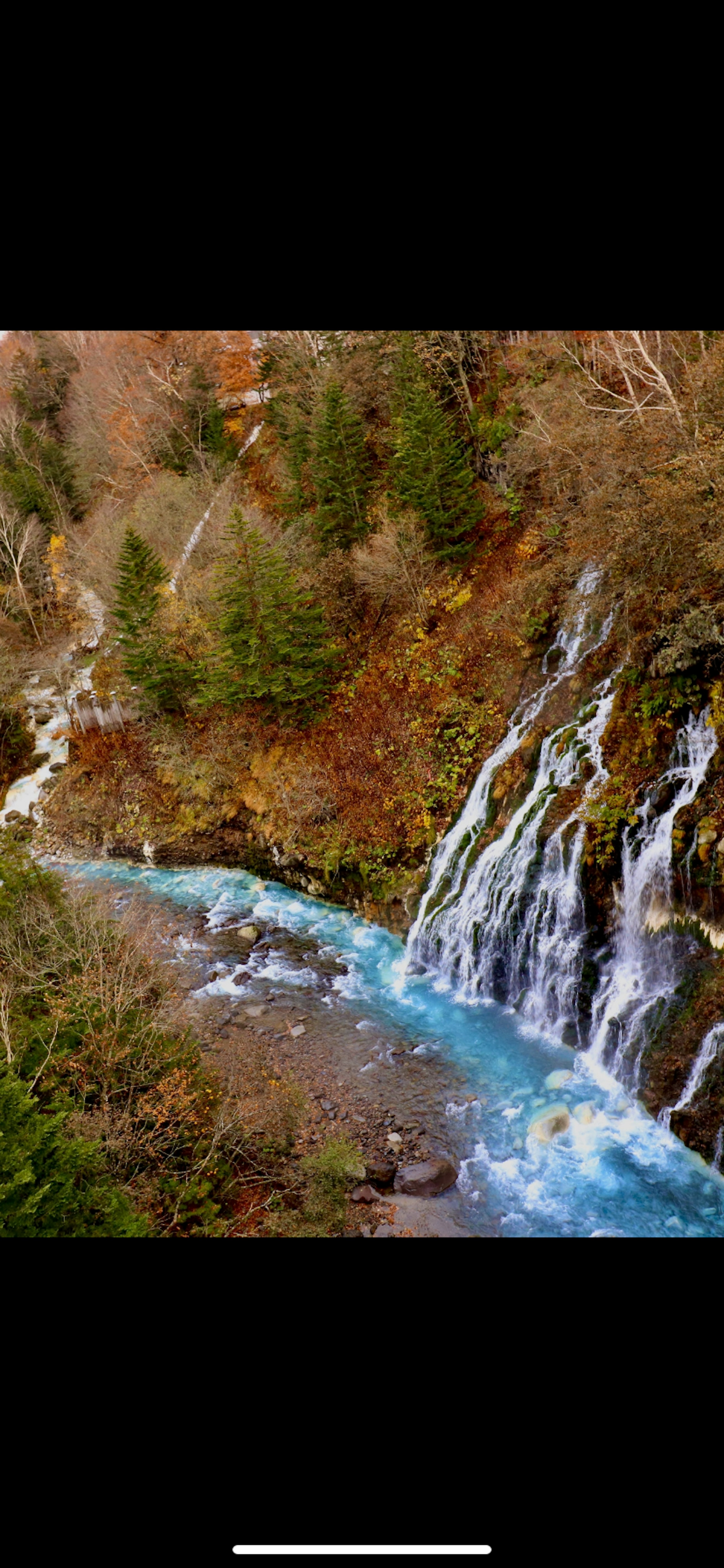 Malersiche Aussicht auf einen blauen Fluss und einen Wasserfall umgeben von herbstlichem Laub