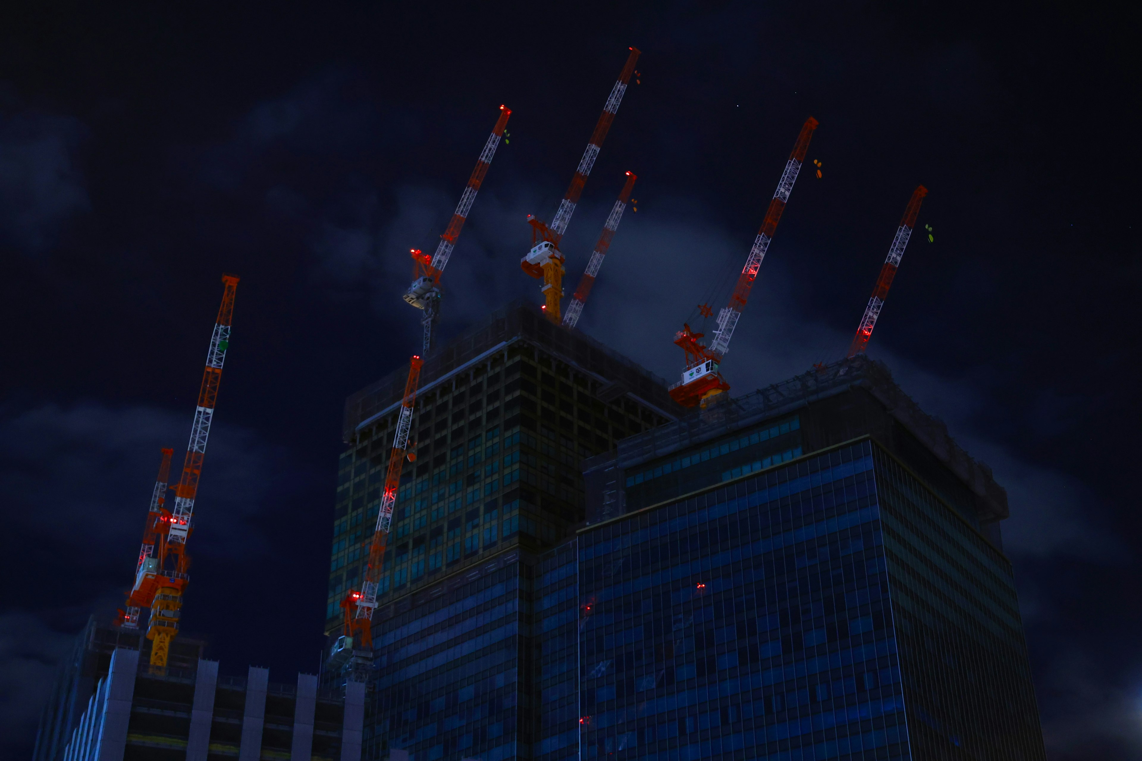 Red and white cranes on top of a skyscraper at night