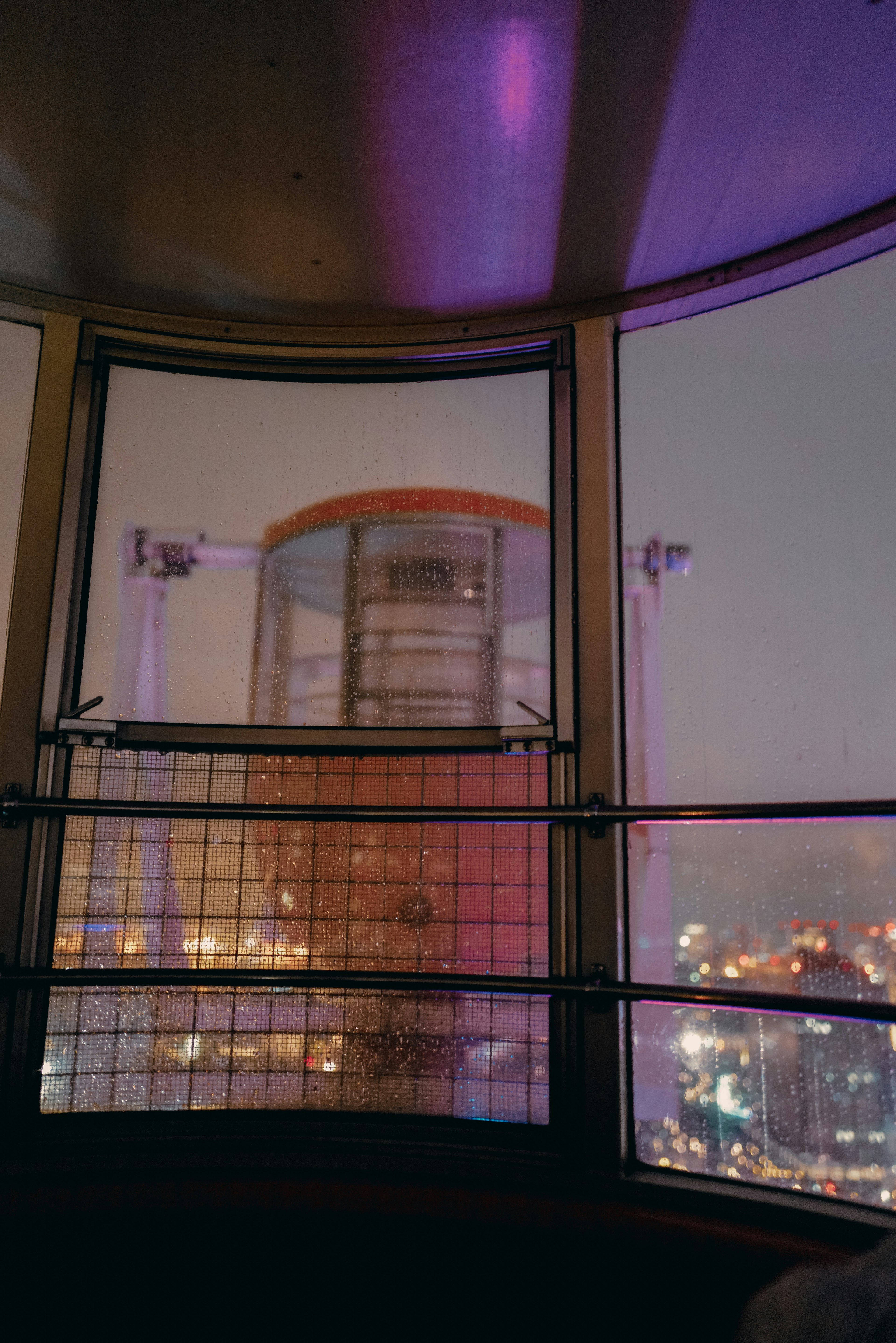 Vista desde el interior de una plataforma de observación que muestra las luces de la ciudad y una iluminación colorida por la noche