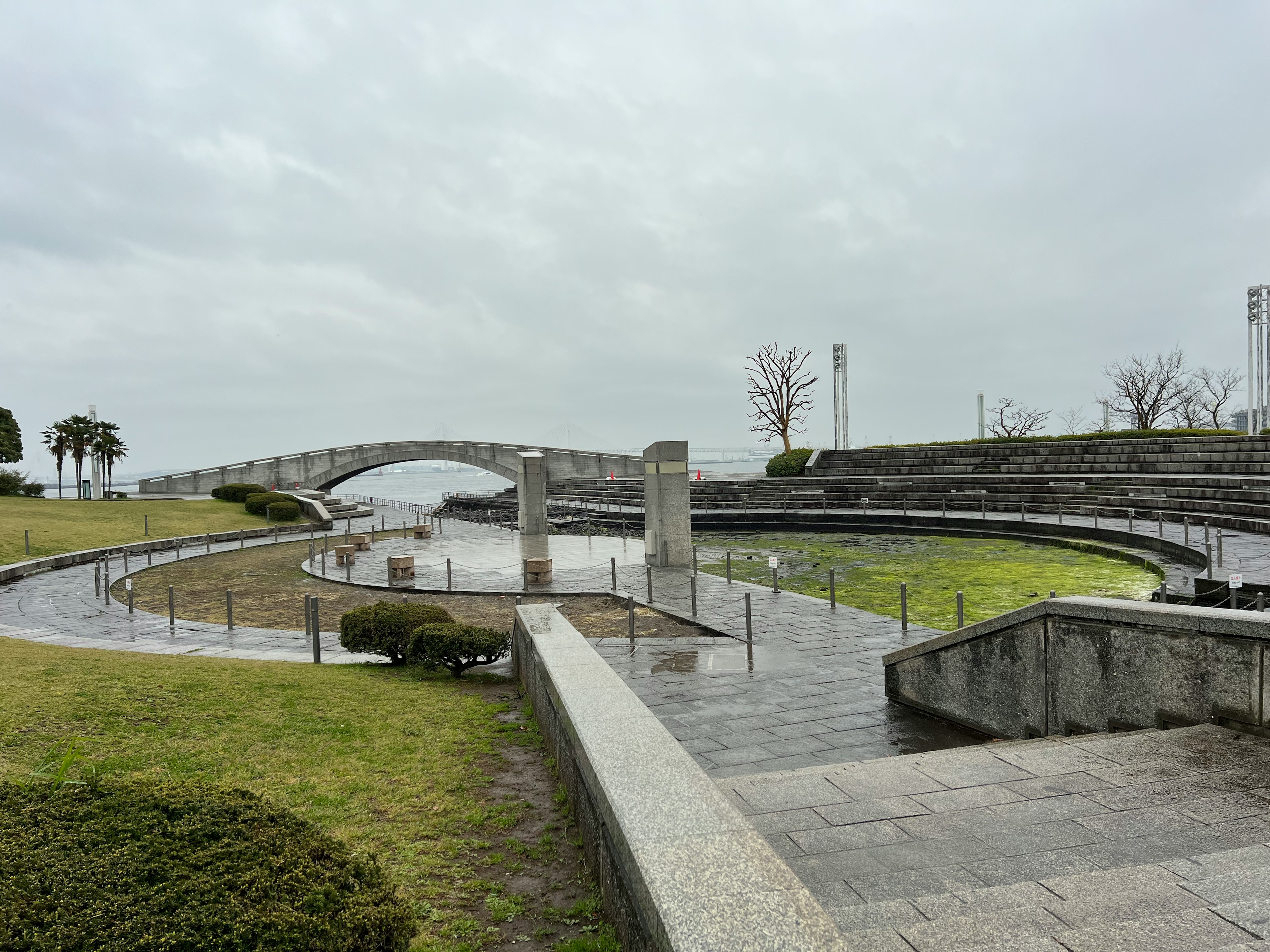 ทิวทัศน์สวนที่เงียบสงบมีสะพานและพื้นที่น้ำทางหญ้าและโครงสร้างหิน