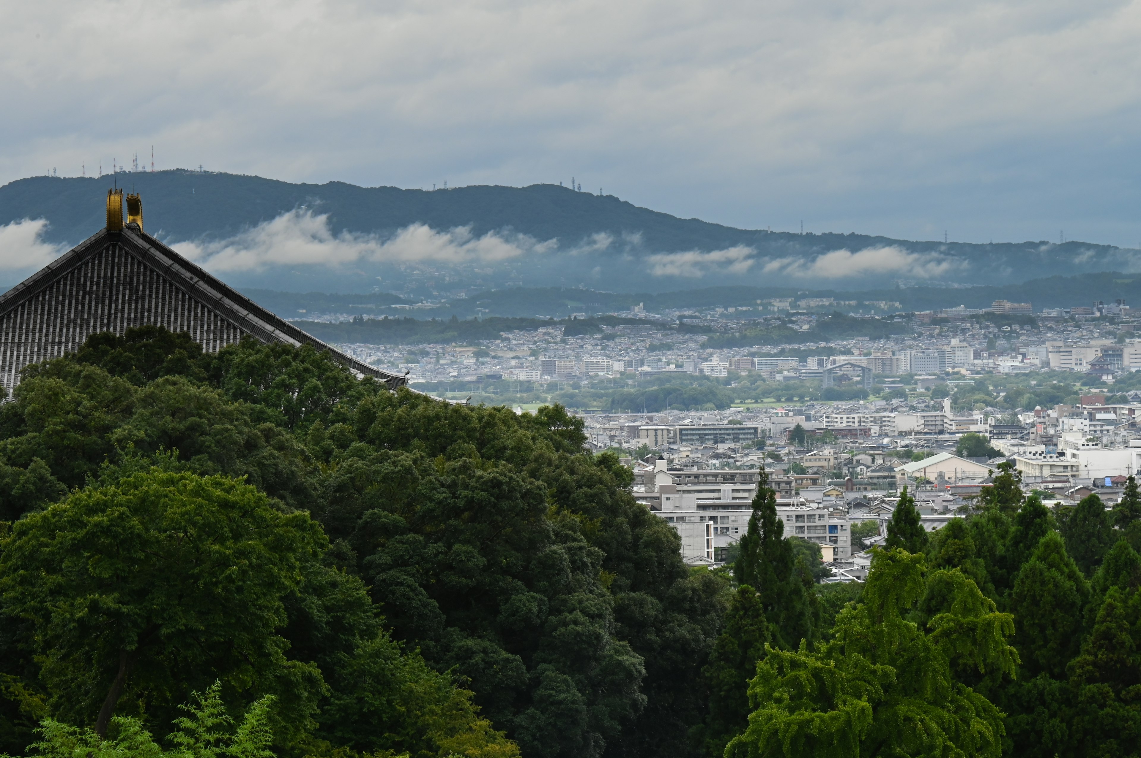 Vista escénica con montañas cubiertas de nubes y vegetación exuberante con un vistazo de un techo de Kioto