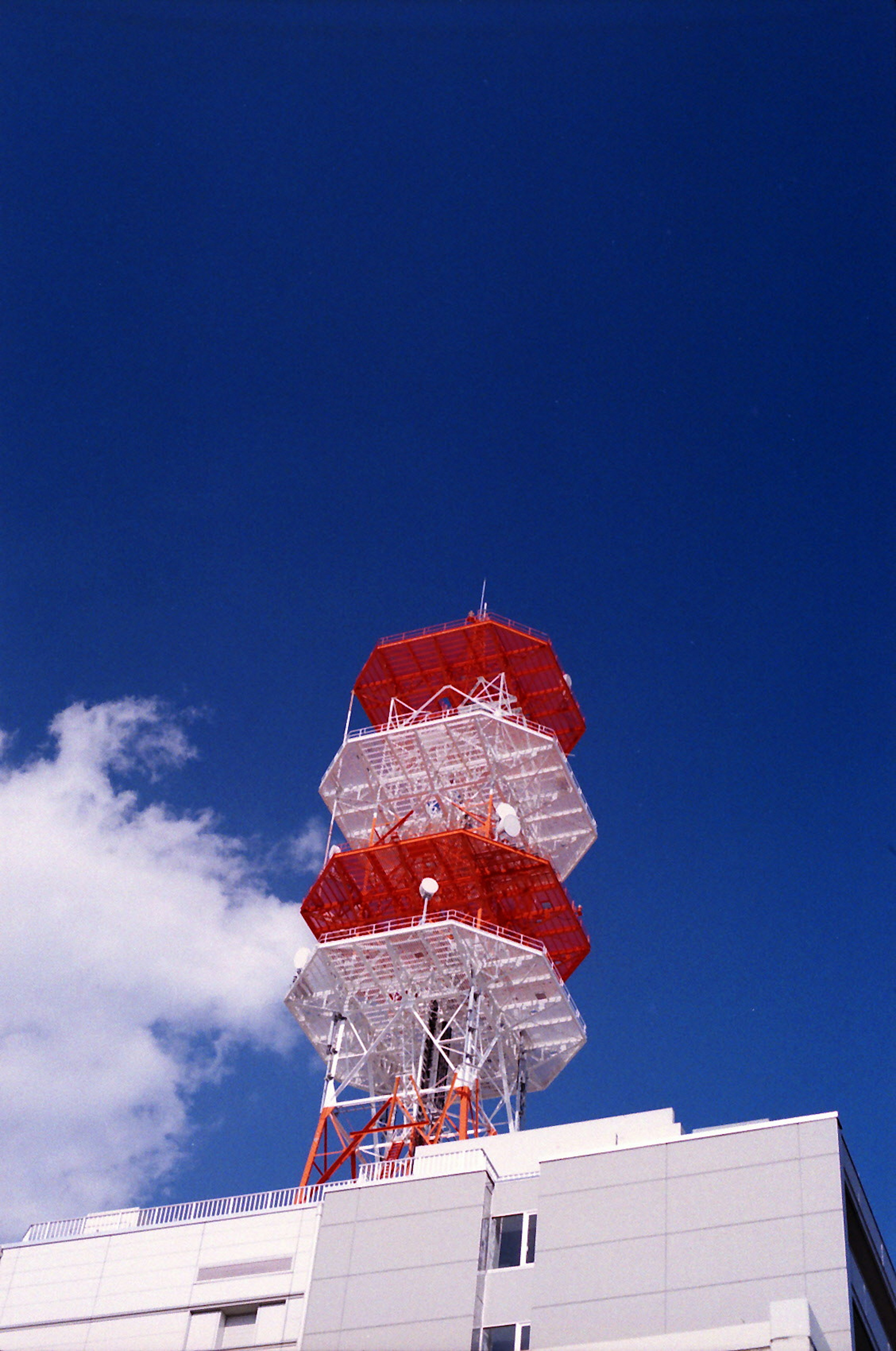 Red and white communication tower rising against a blue sky