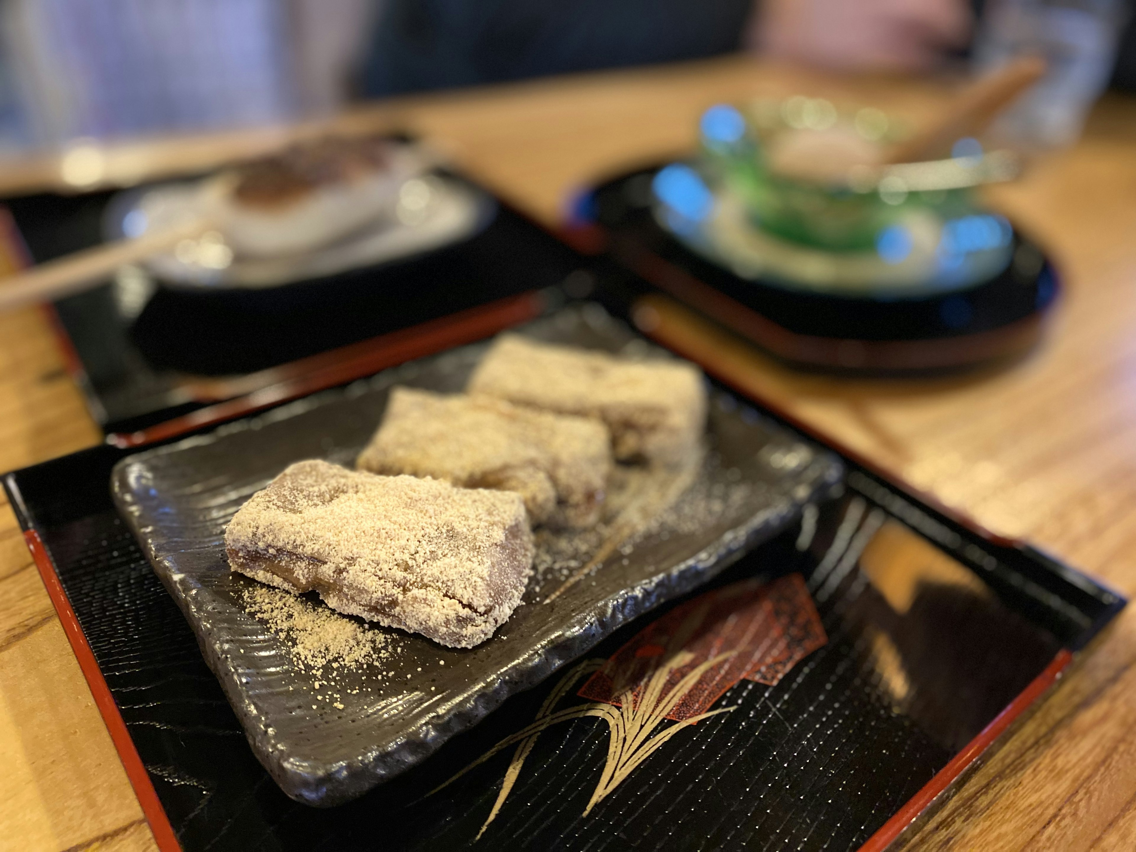 Mochi de kinako servido en un plato negro con una mesa de madera al fondo