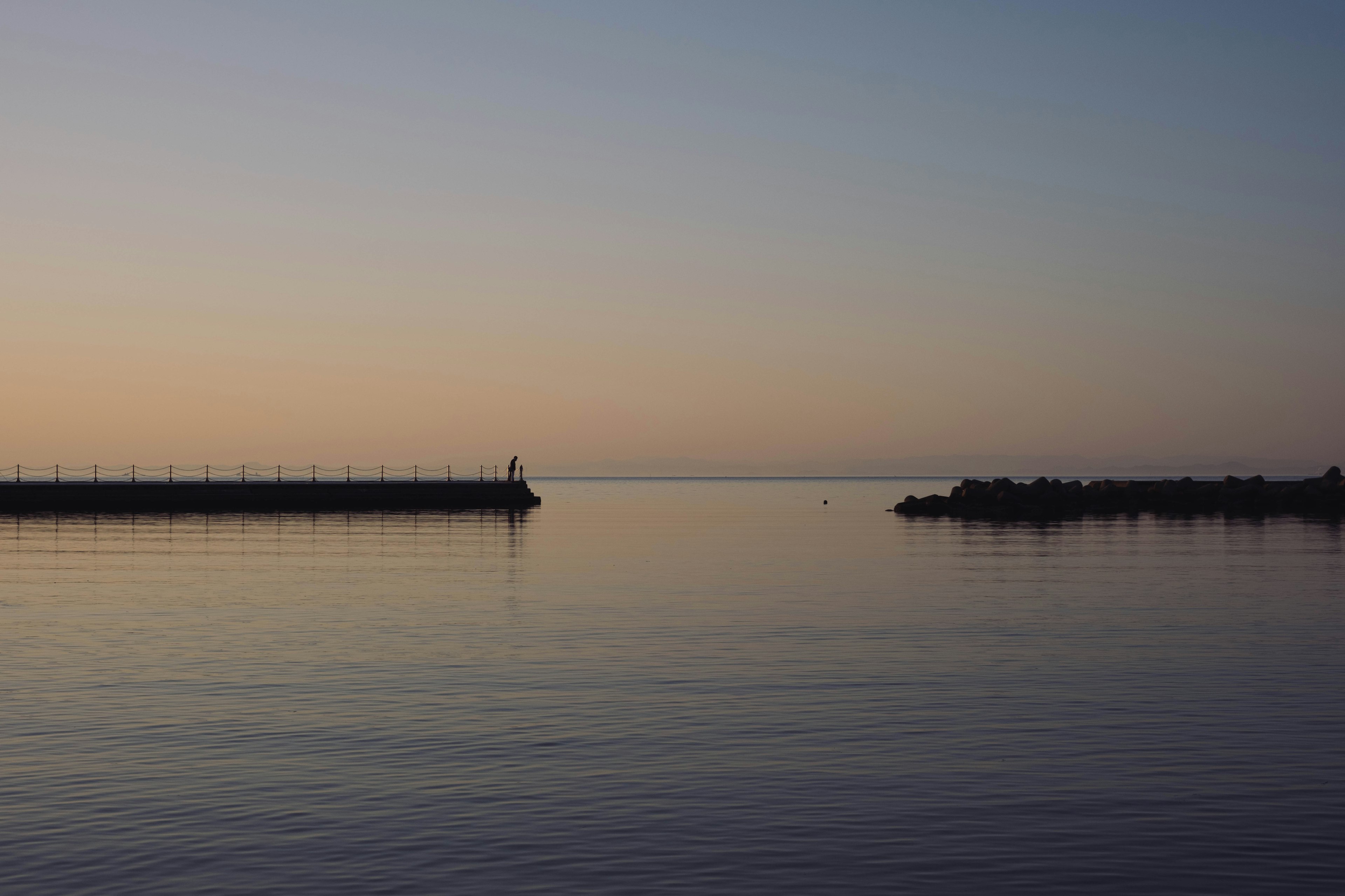 Ruhiges Wasser, das den Abendhimmel und die Silhouette eines Wellenbrechers spiegelt