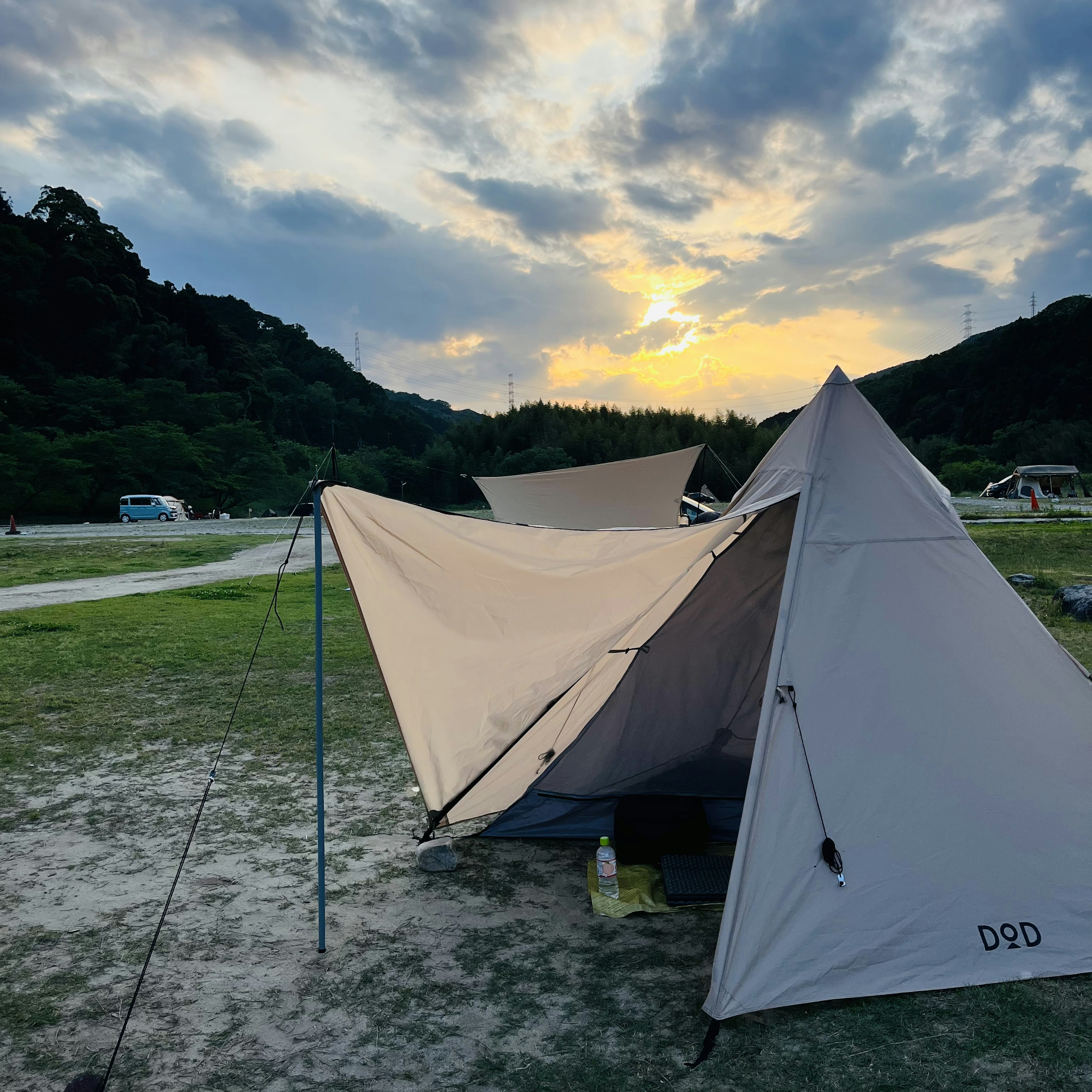 Tenda yang berdiri di bawah matahari terbenam dengan alam sekitar