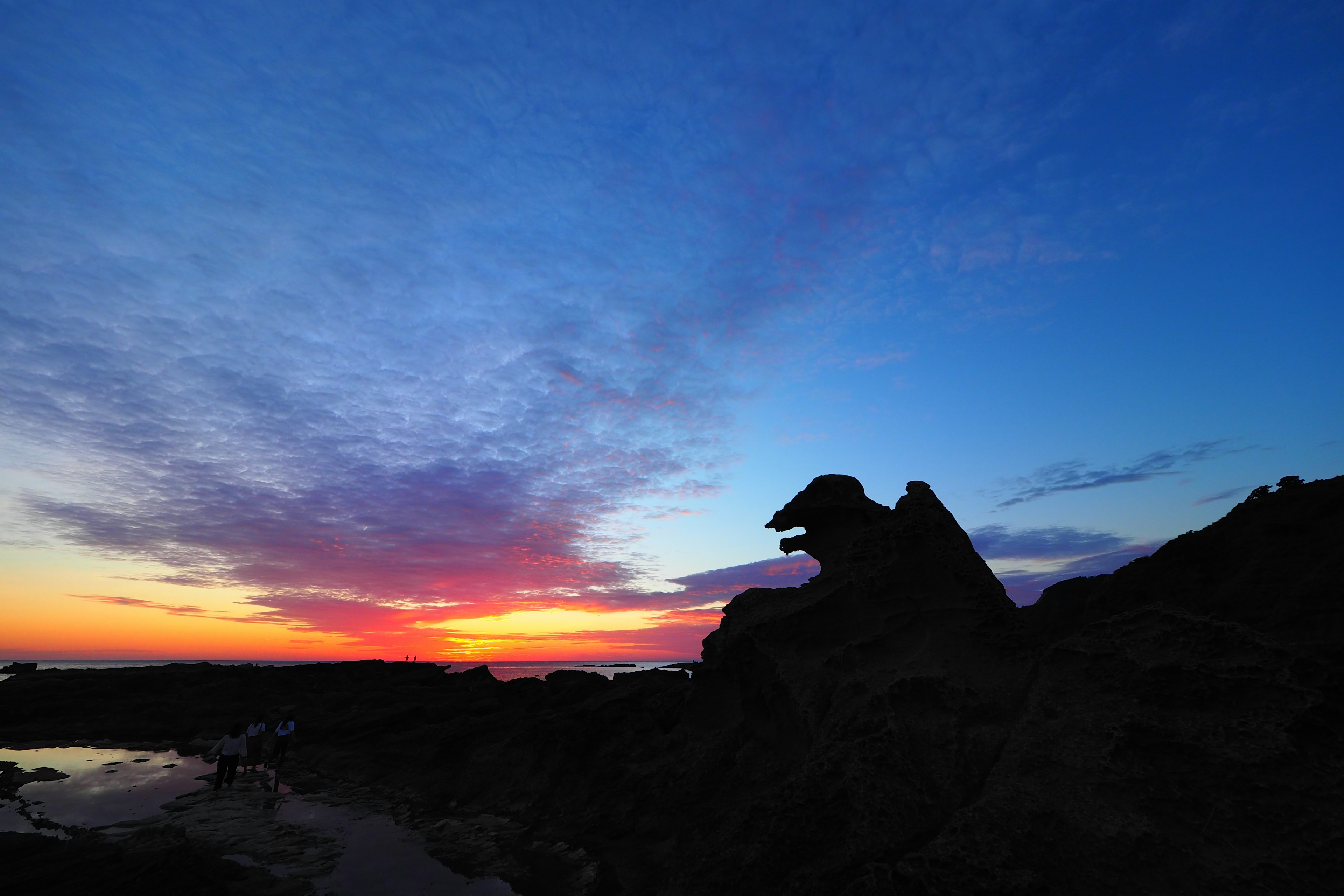 Silhouette einer Felsformation, die einem Tier ähnelt, vor einem bunten Sonnenuntergangshimmel