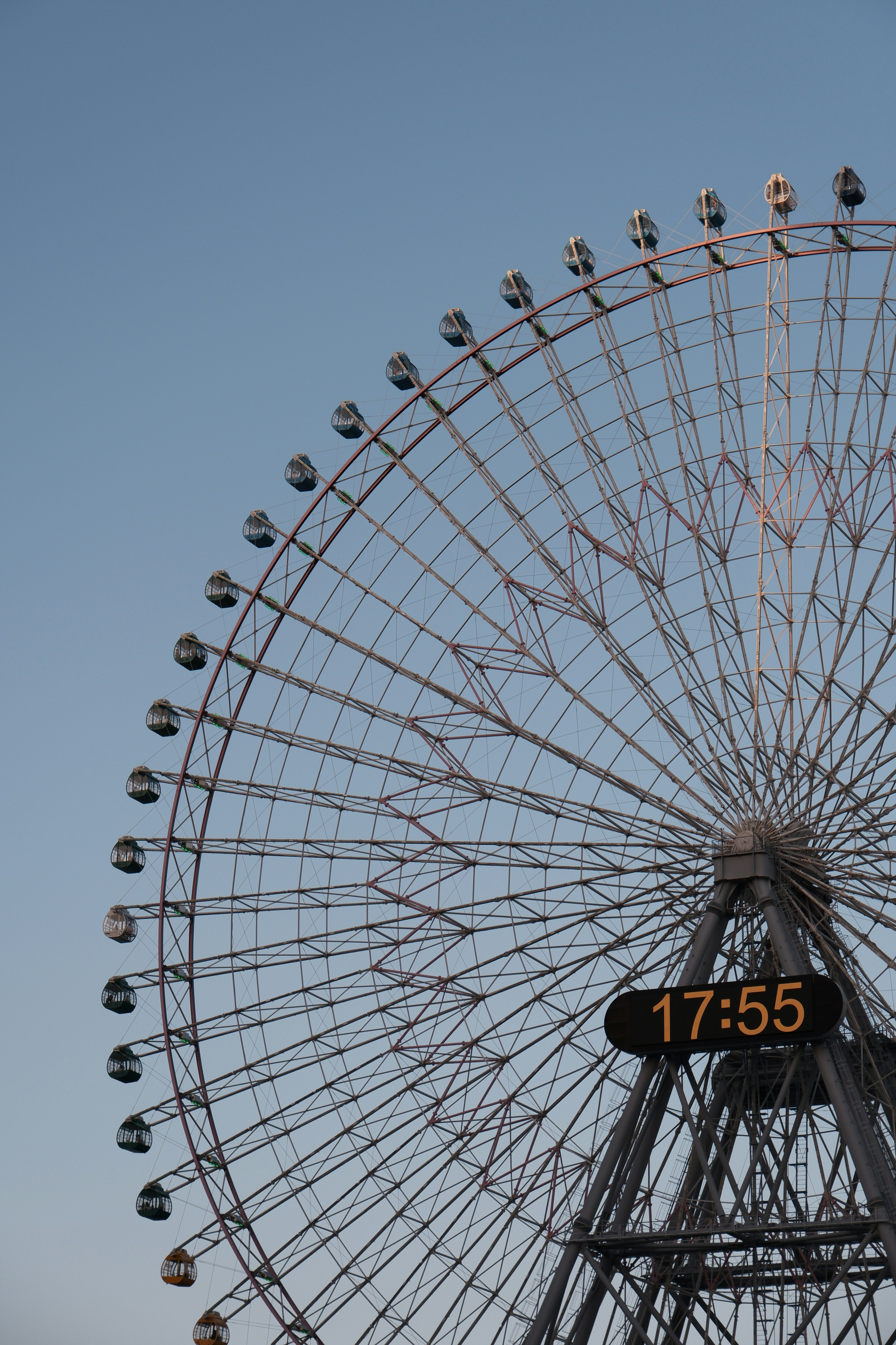 Parte di una ruota panoramica contro un cielo blu che mostra l'ora 17:55