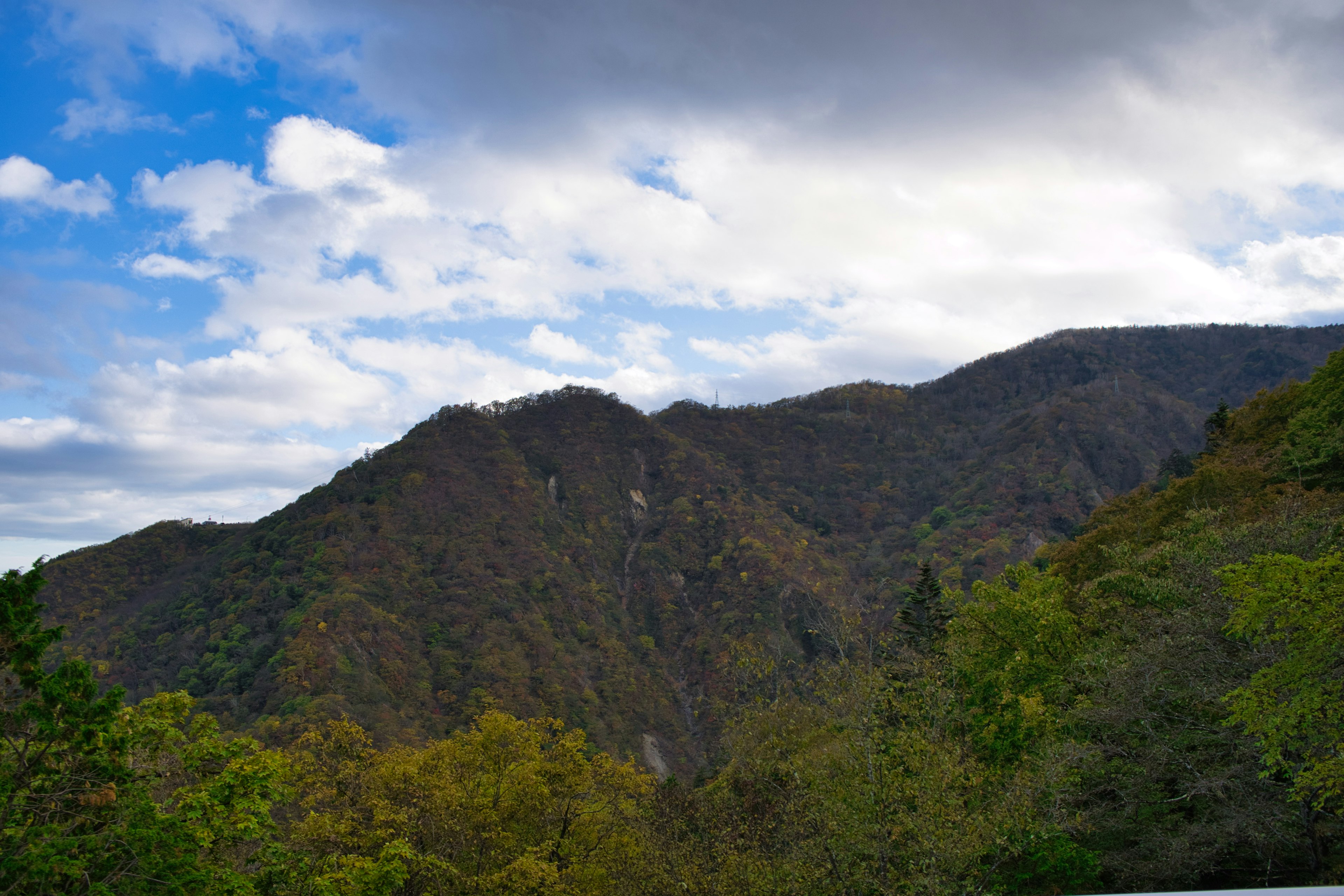 被蓝天和云朵环绕的山景 有绿色树木和秋季色彩