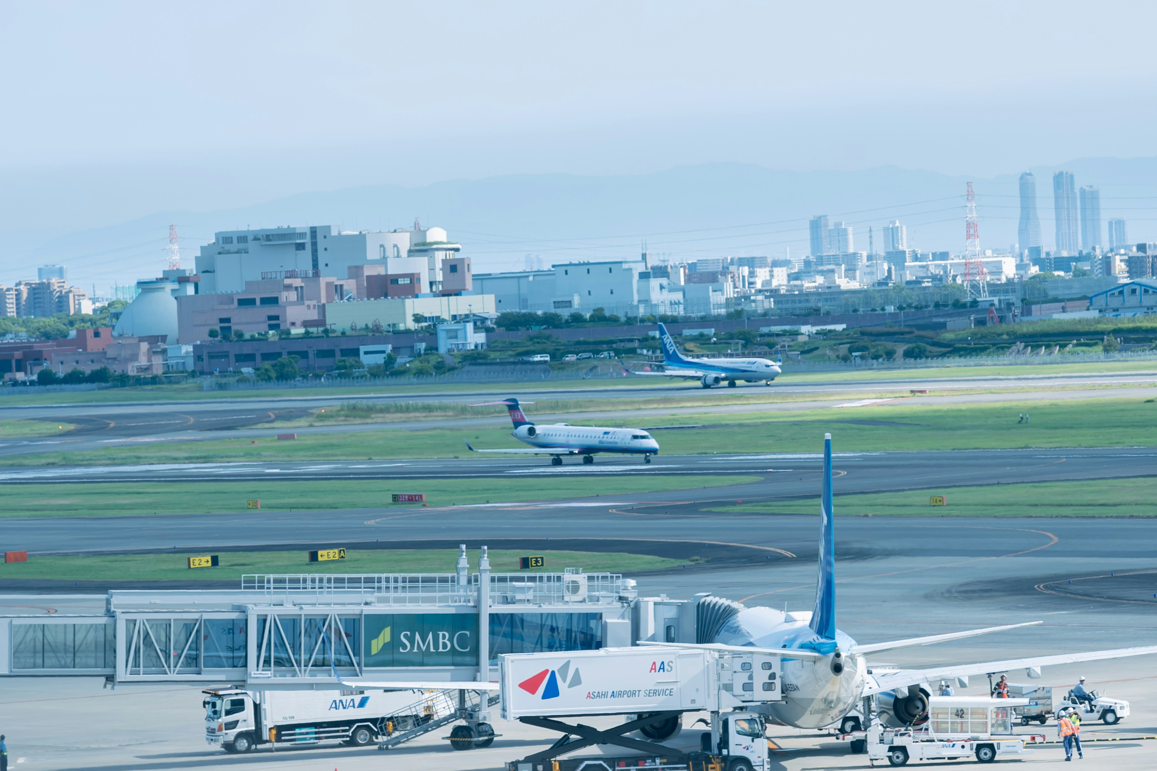 Multiple airplanes on an airport runway with a city skyline in the background