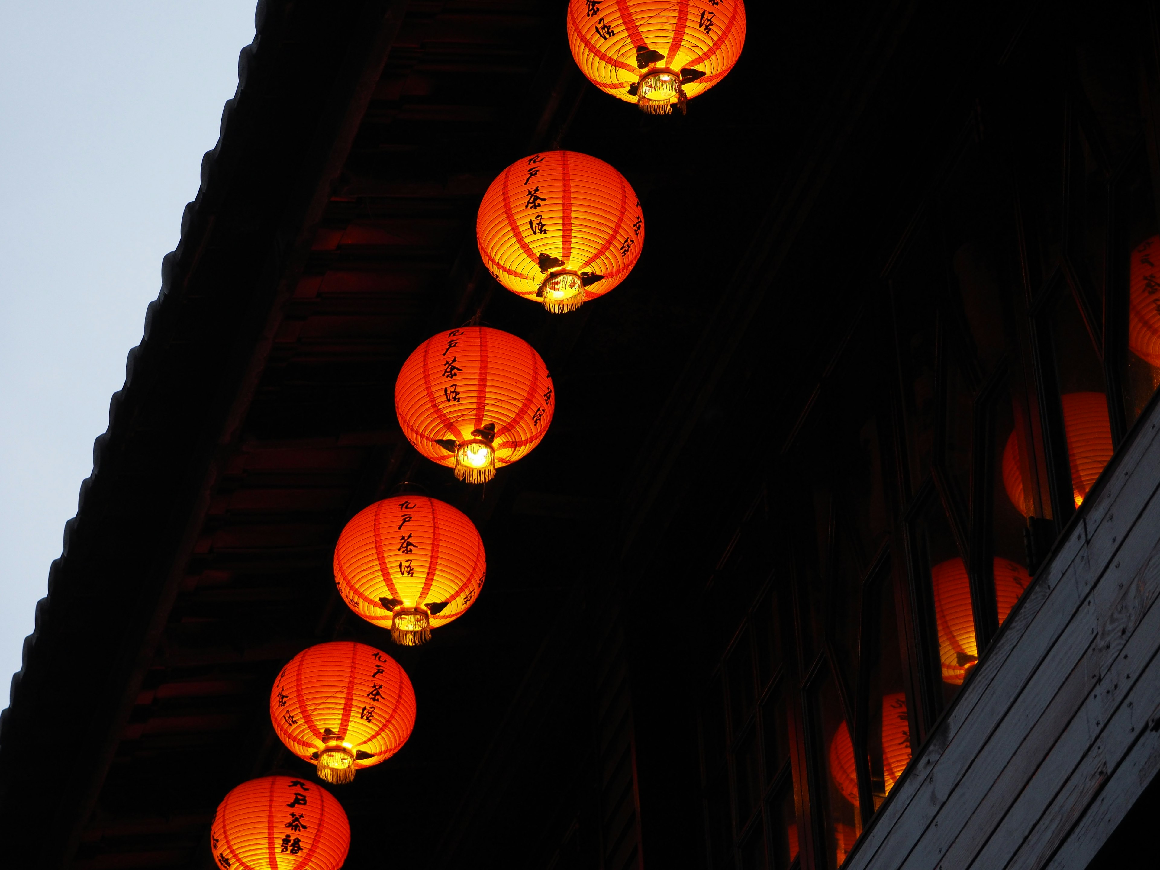 Row of bright orange lanterns hanging from a building roof