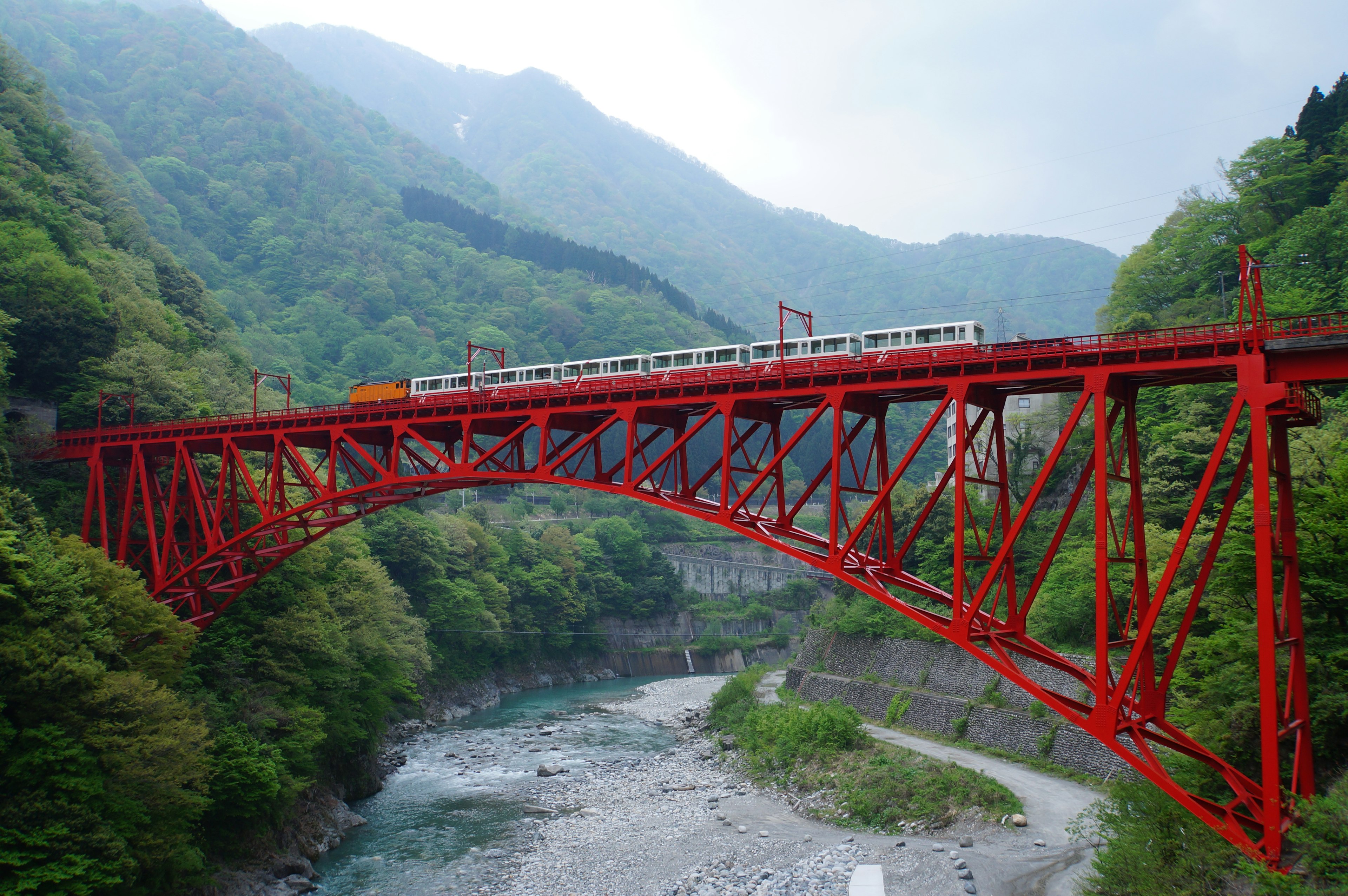 Un pont en treillis rouge avec un train le traversant entouré de montagnes verdoyantes