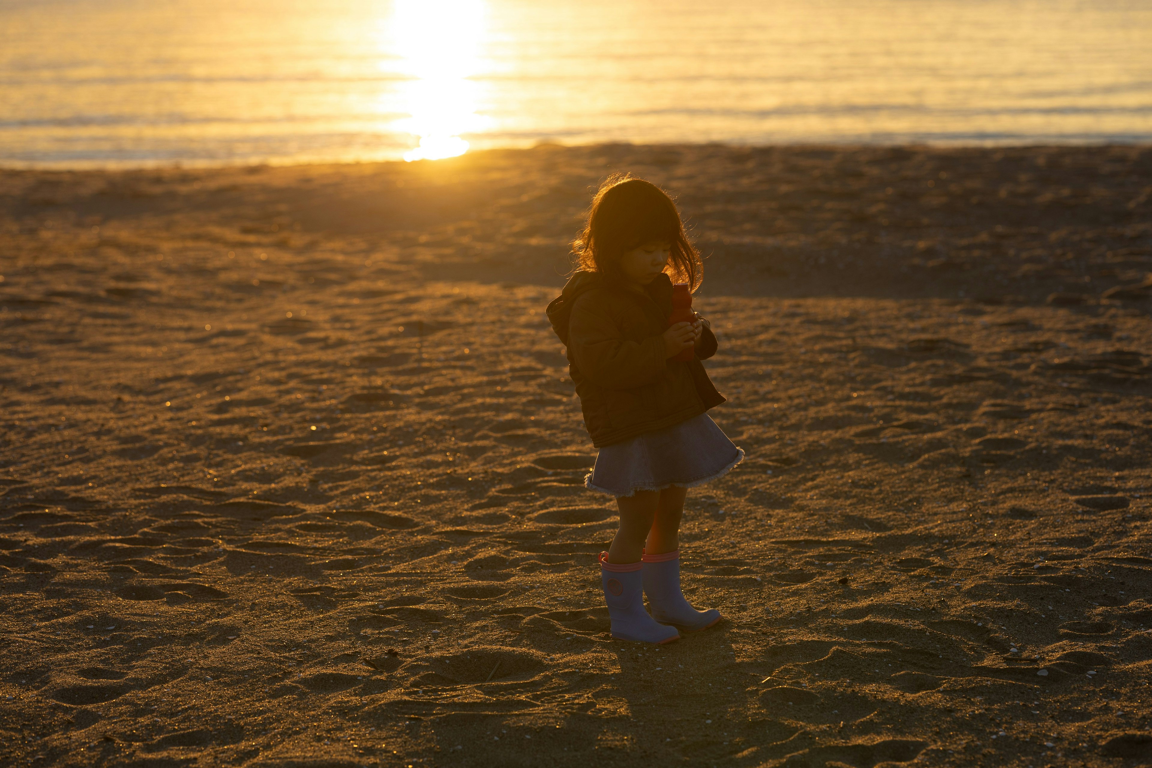Silhouette d'un enfant se tenant sur la plage avec le coucher de soleil en arrière-plan
