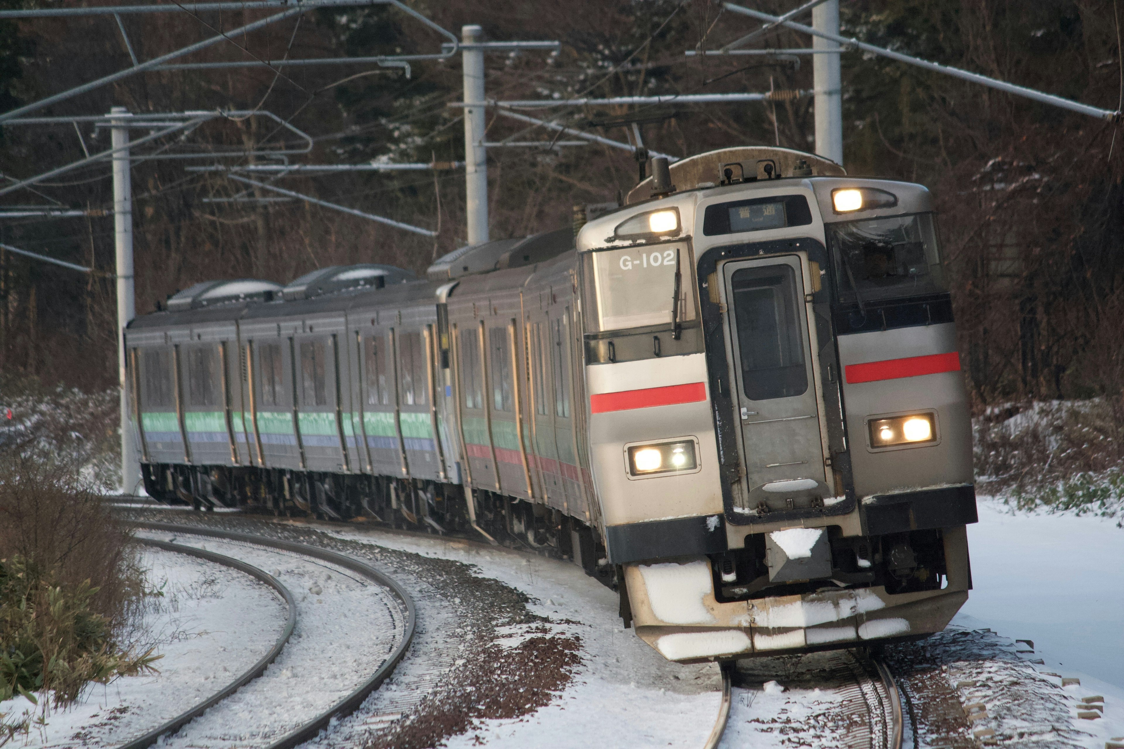 Zug, der in den Schnee fährt, mit sichtbaren Gleisen und Oberleitungen