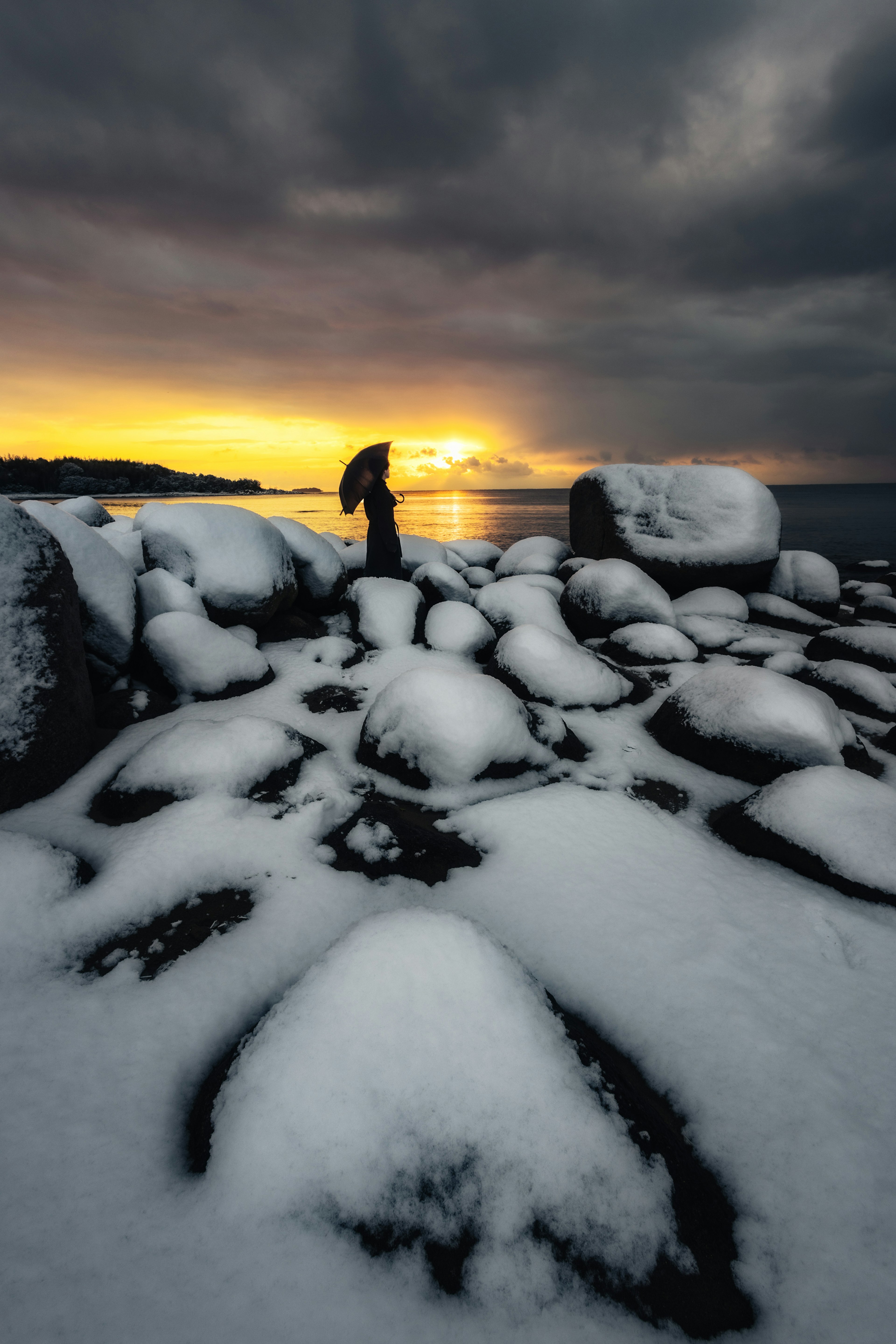 Persona de pie sobre rocas cubiertas de nieve con el atardecer de fondo