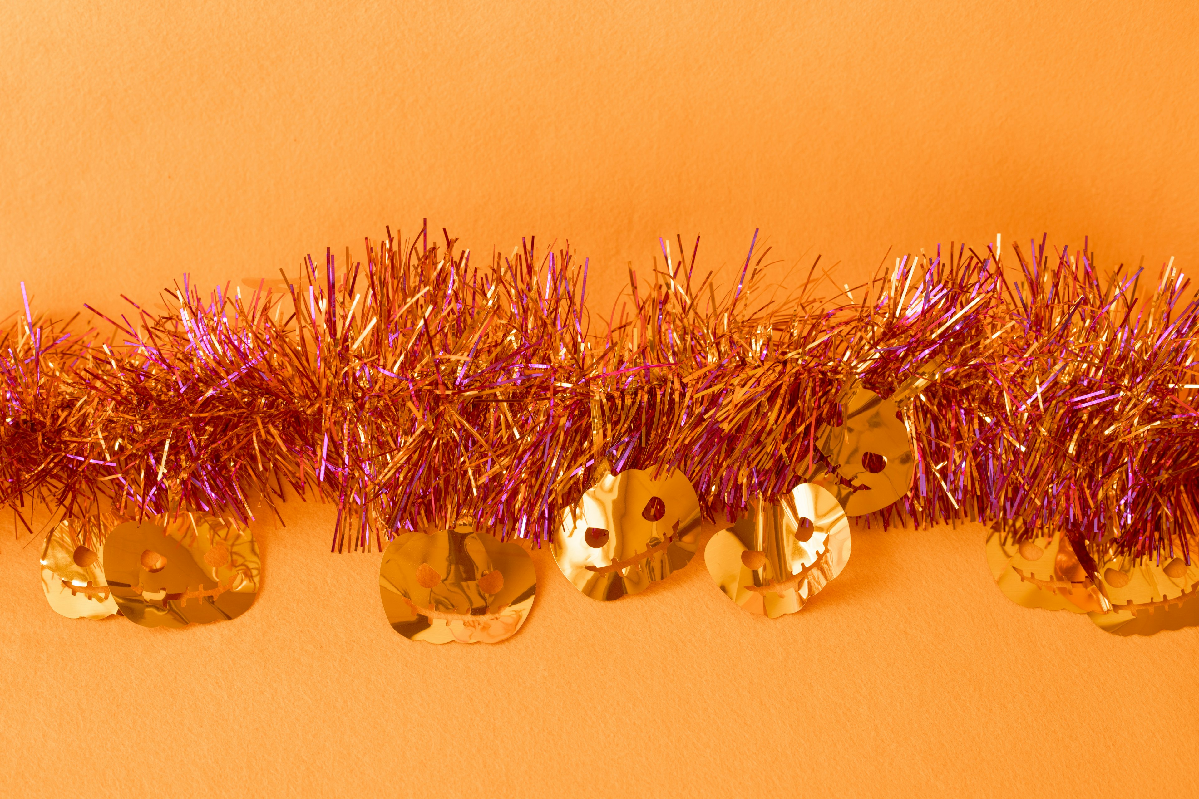 A festive decoration with gold bells and purple tinsel on an orange background