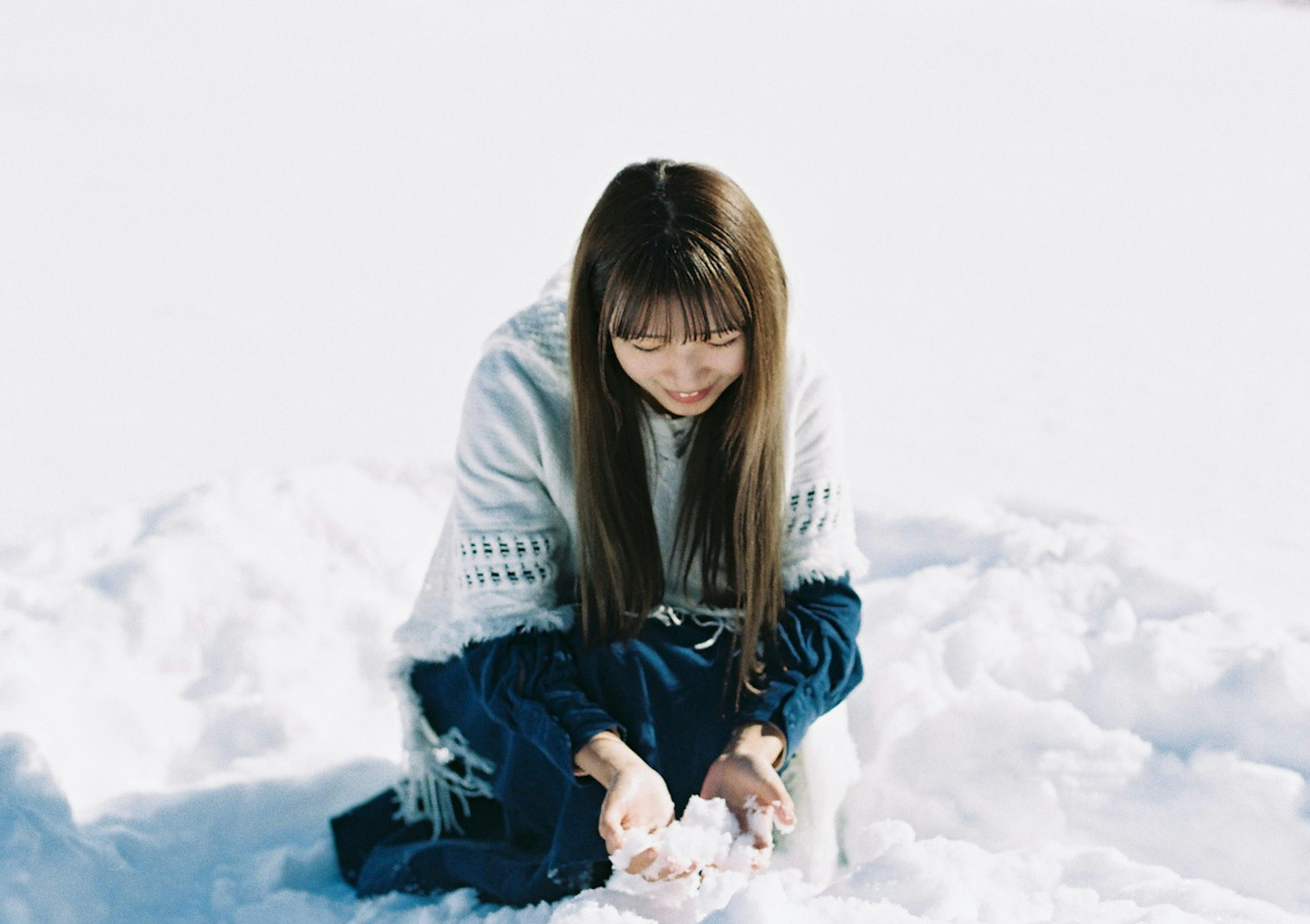 Una mujer jugando en la nieve con cabello largo usando un suéter blanco y sonriendo