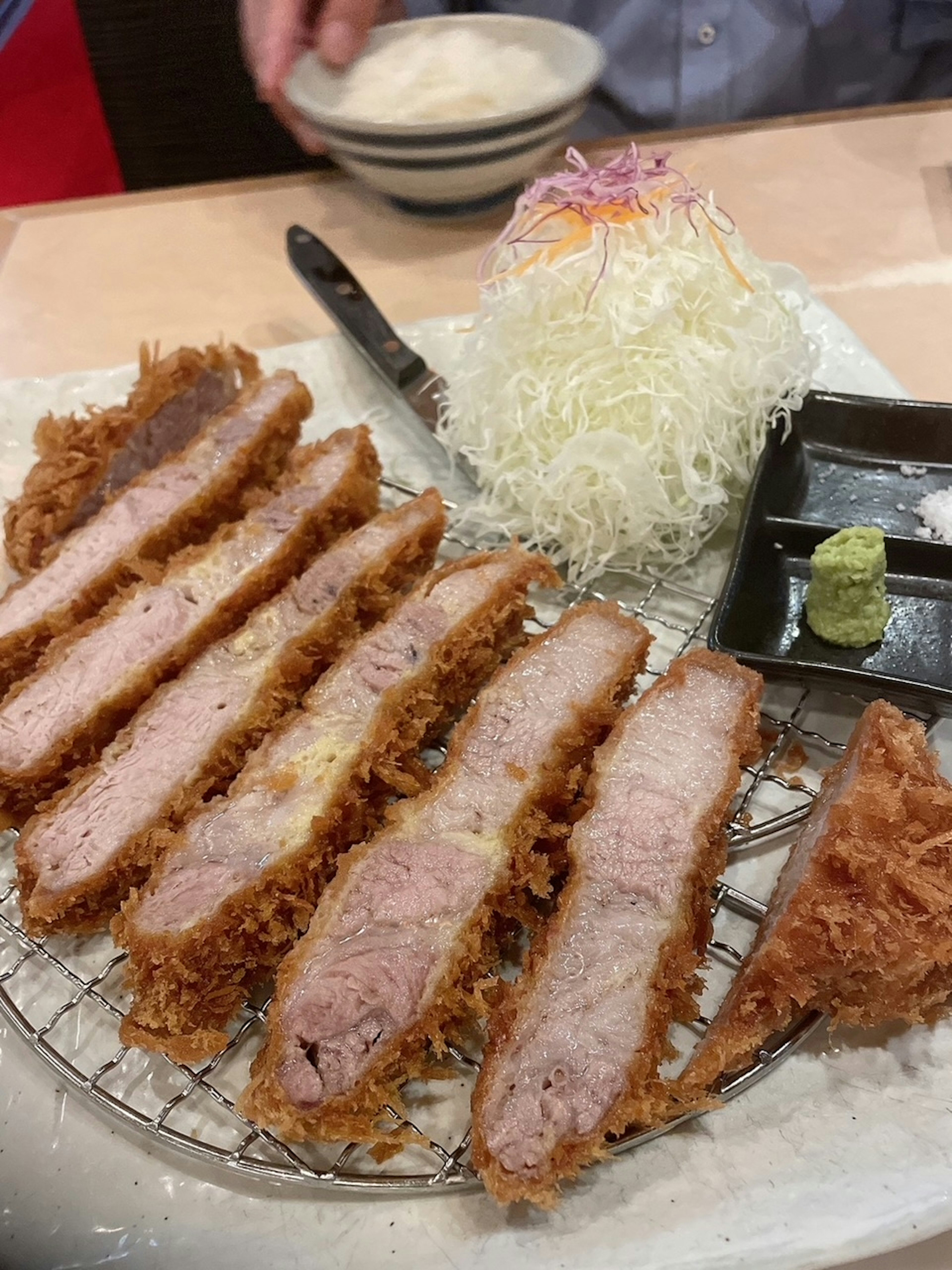 In Scheiben geschnittenes Tonkatsu auf einem Teller mit gehobeltem Kohl und Wasabi