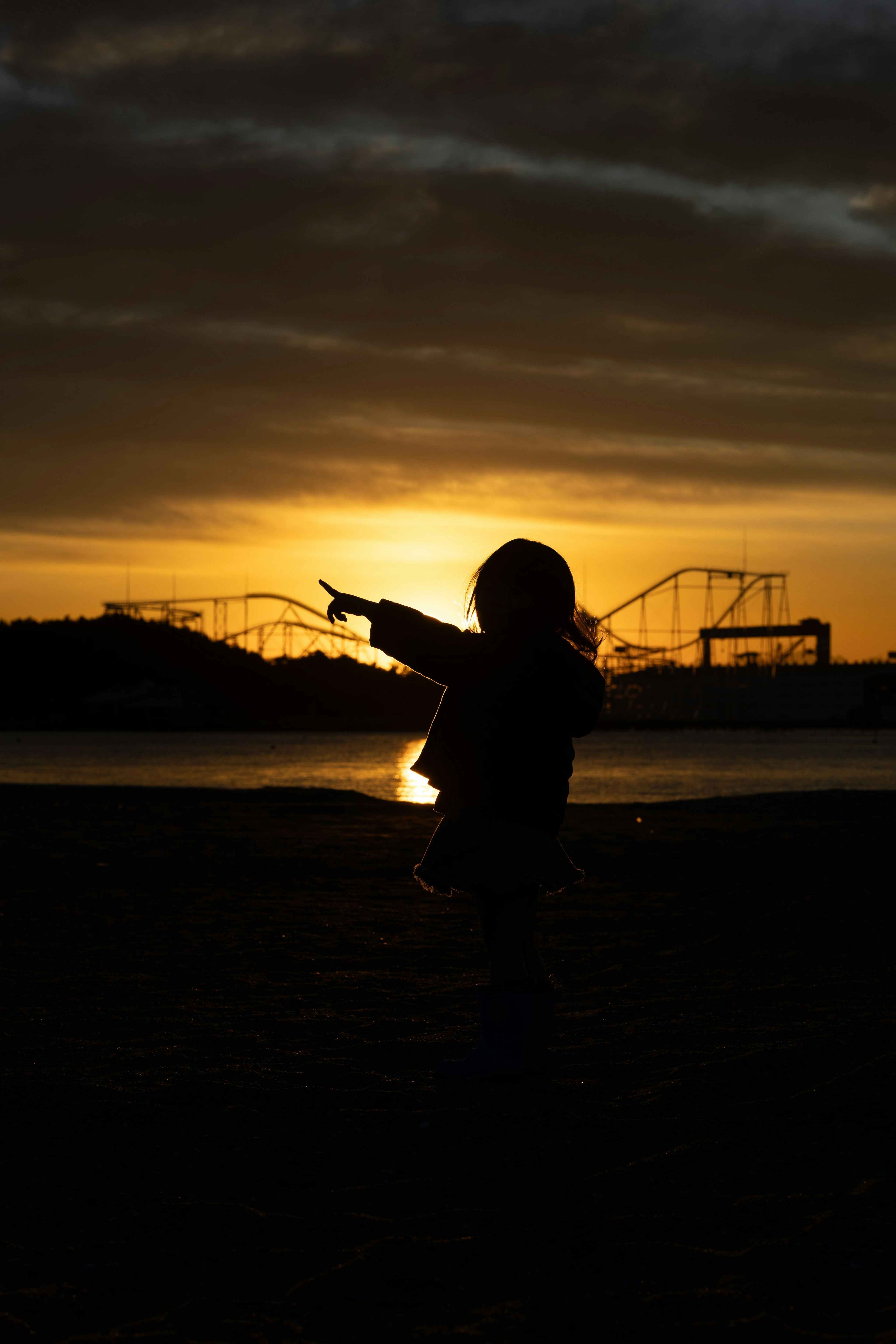 Silhouette d'un enfant pointant contre un coucher de soleil avec des montagnes russes en arrière-plan