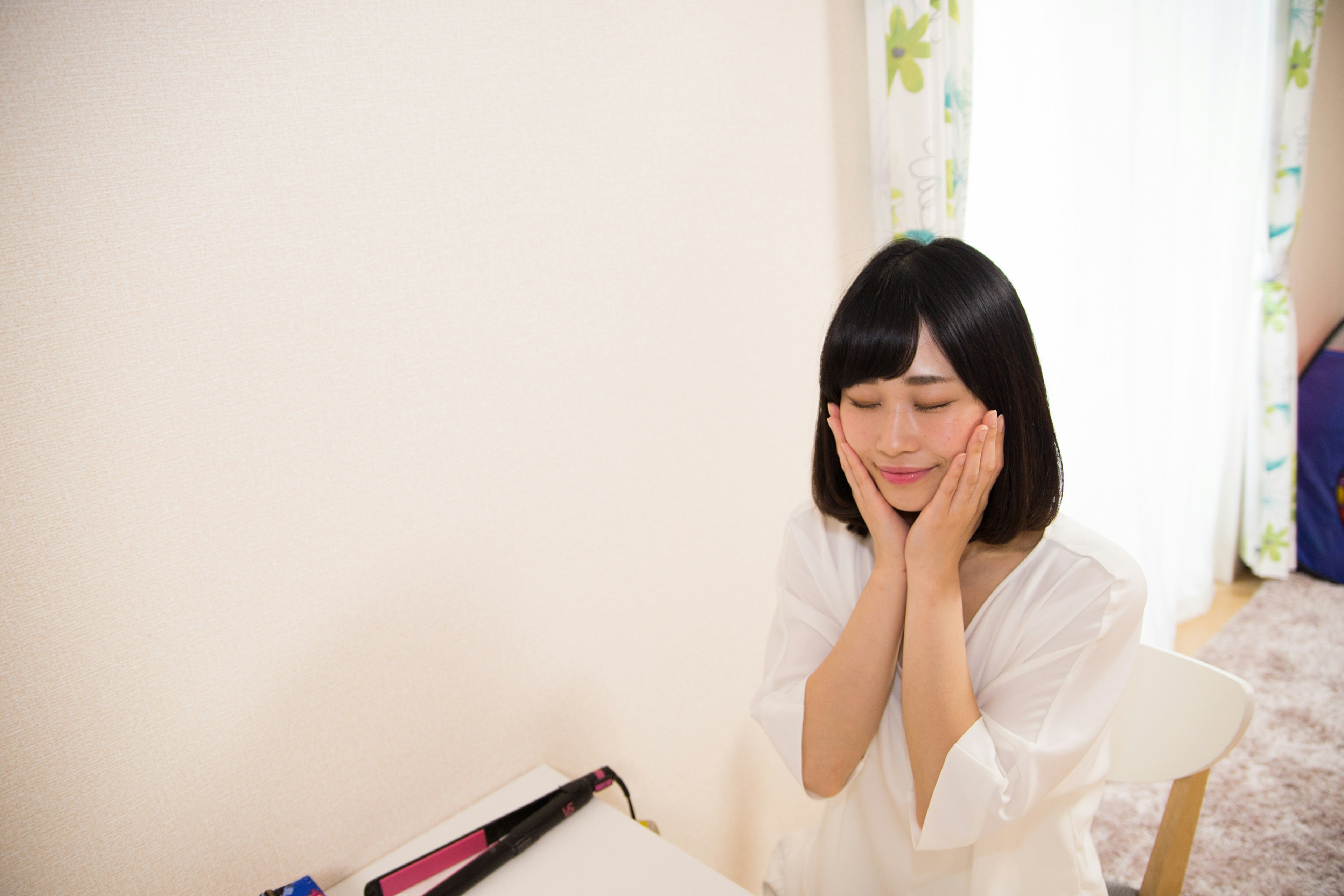 Una donna in abito bianco sorridente con le mani sul viso in una stanza luminosa