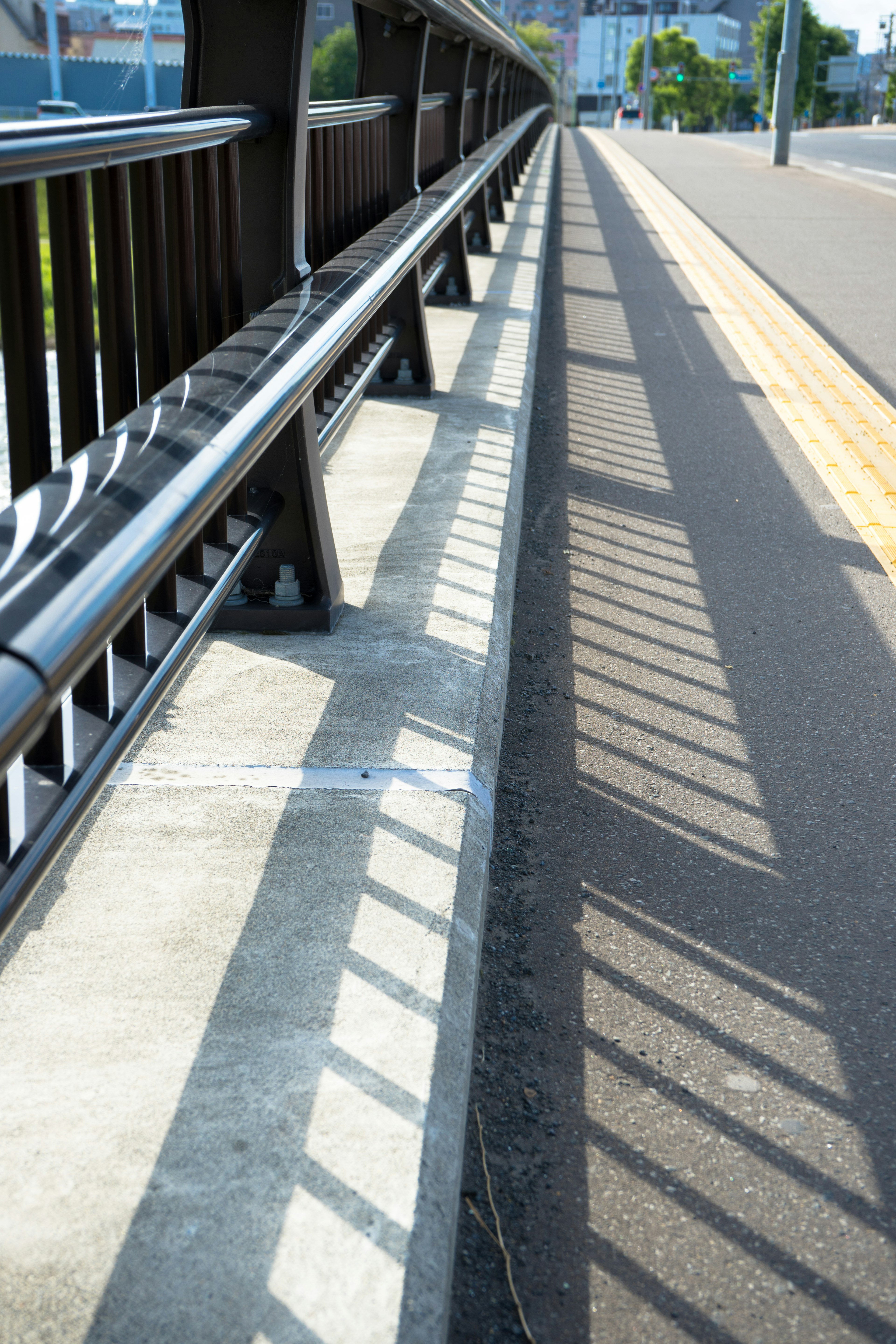 Bürgersteig mit Geländer und Schattenmustern von einer Brücke