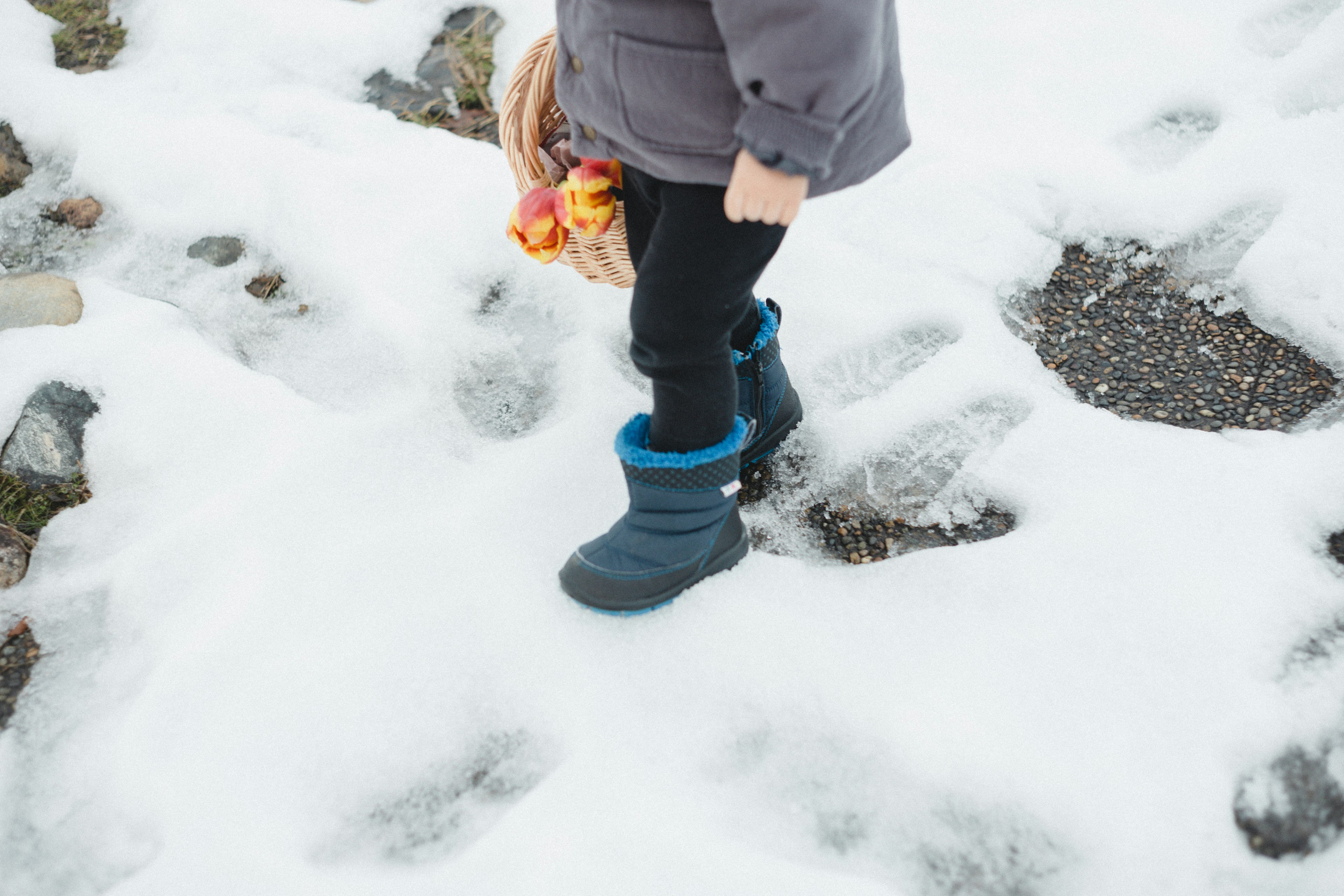 Füße eines Kindes in blauen Stiefeln, die auf Schnee mit bunten Blumen gehen