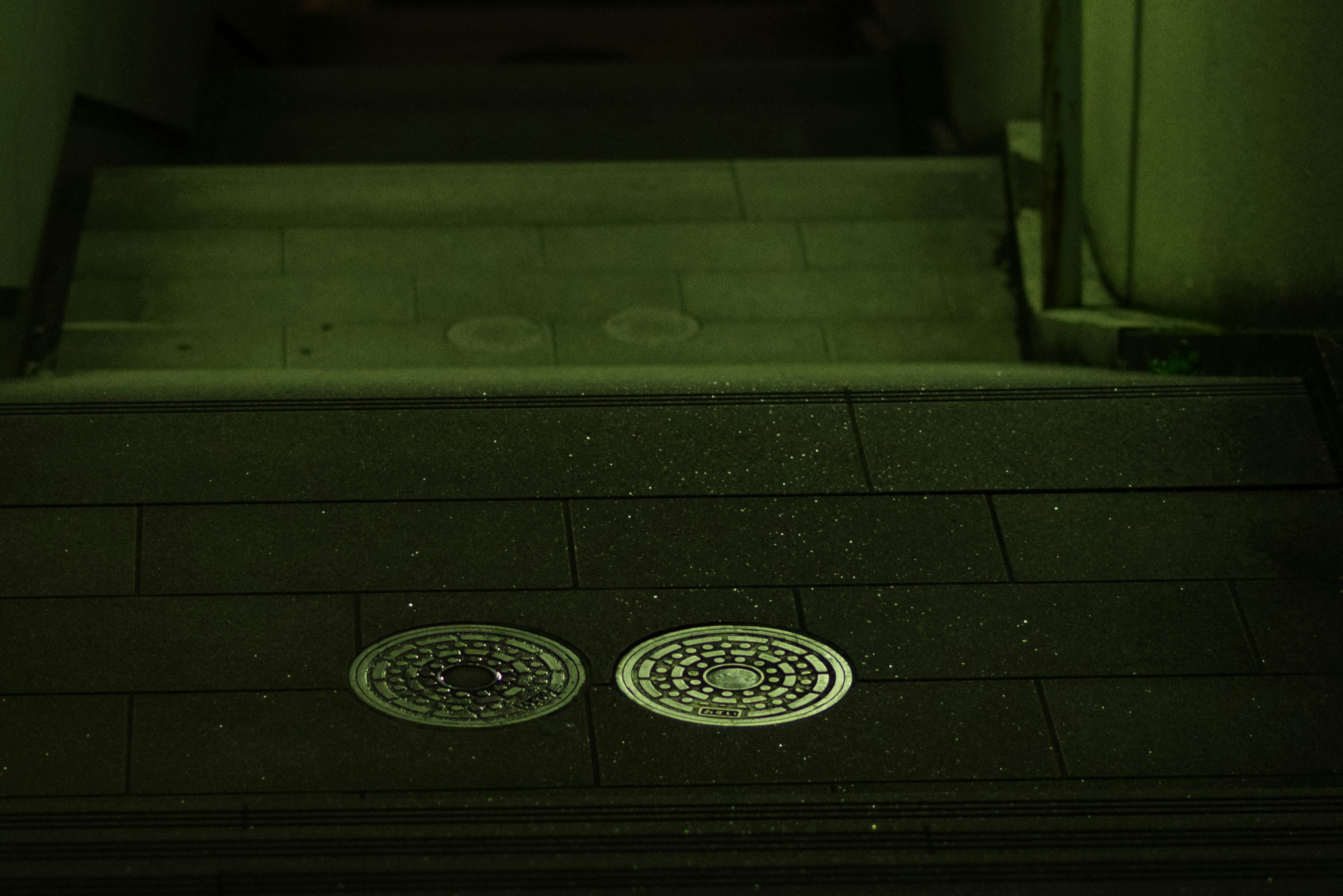 Deux plaques d'égout circulaires sur des escaliers éclairés en vert sombre