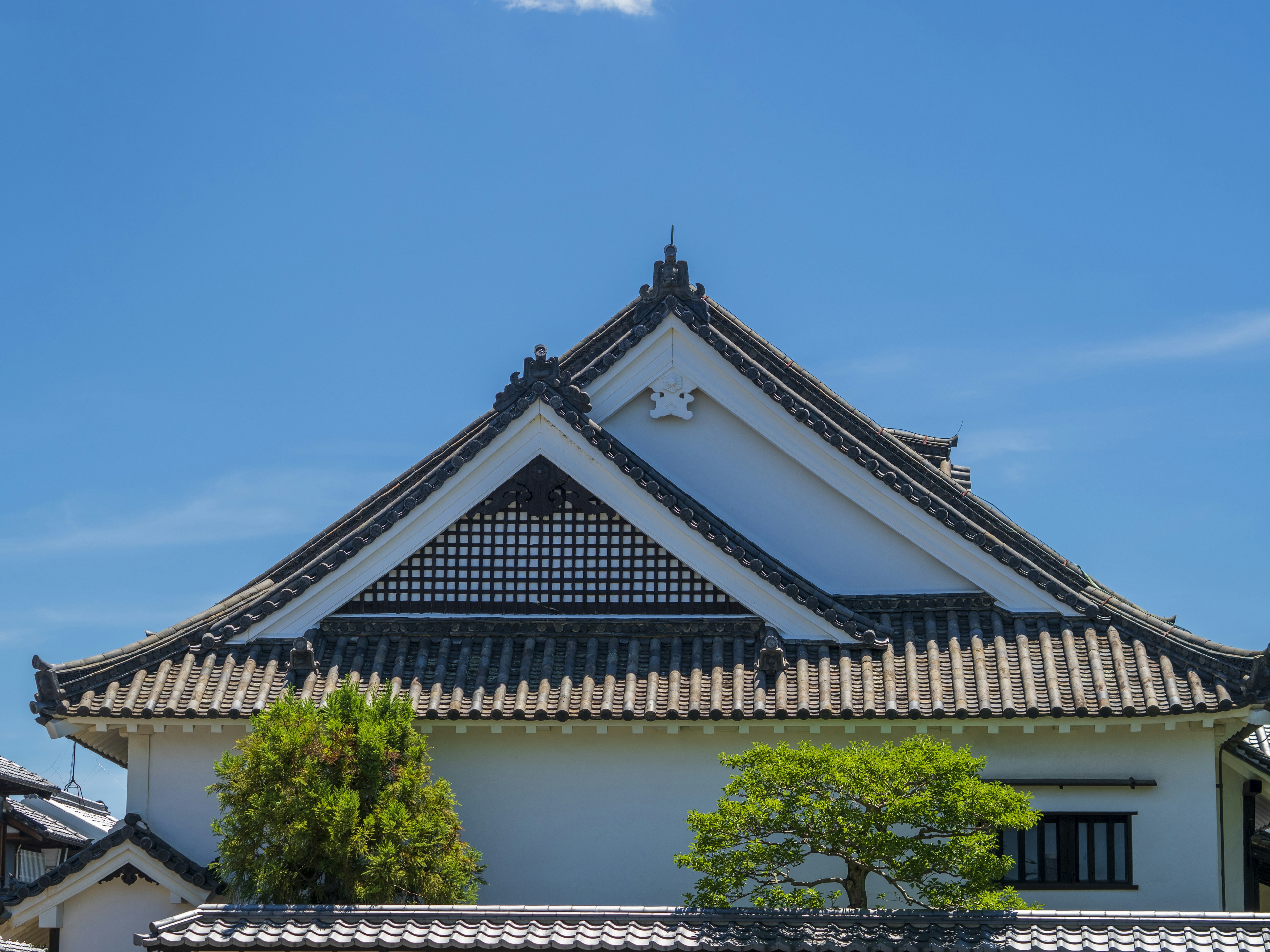 青空の下にある伝統的な日本の建物の屋根と緑の木